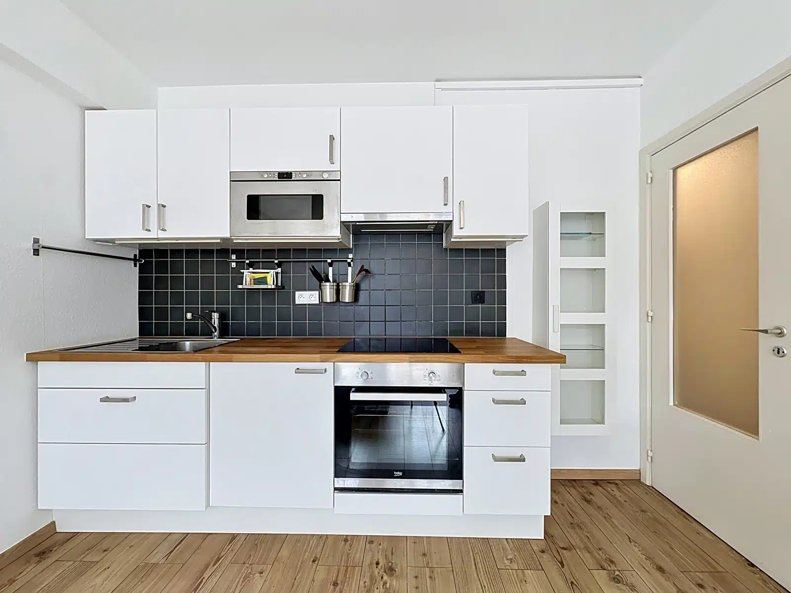 whise photo 3 Modern white kitchen with black tile backsplash, wooden countertop, and stainless appliances (oven, microwave) under wall cabinets