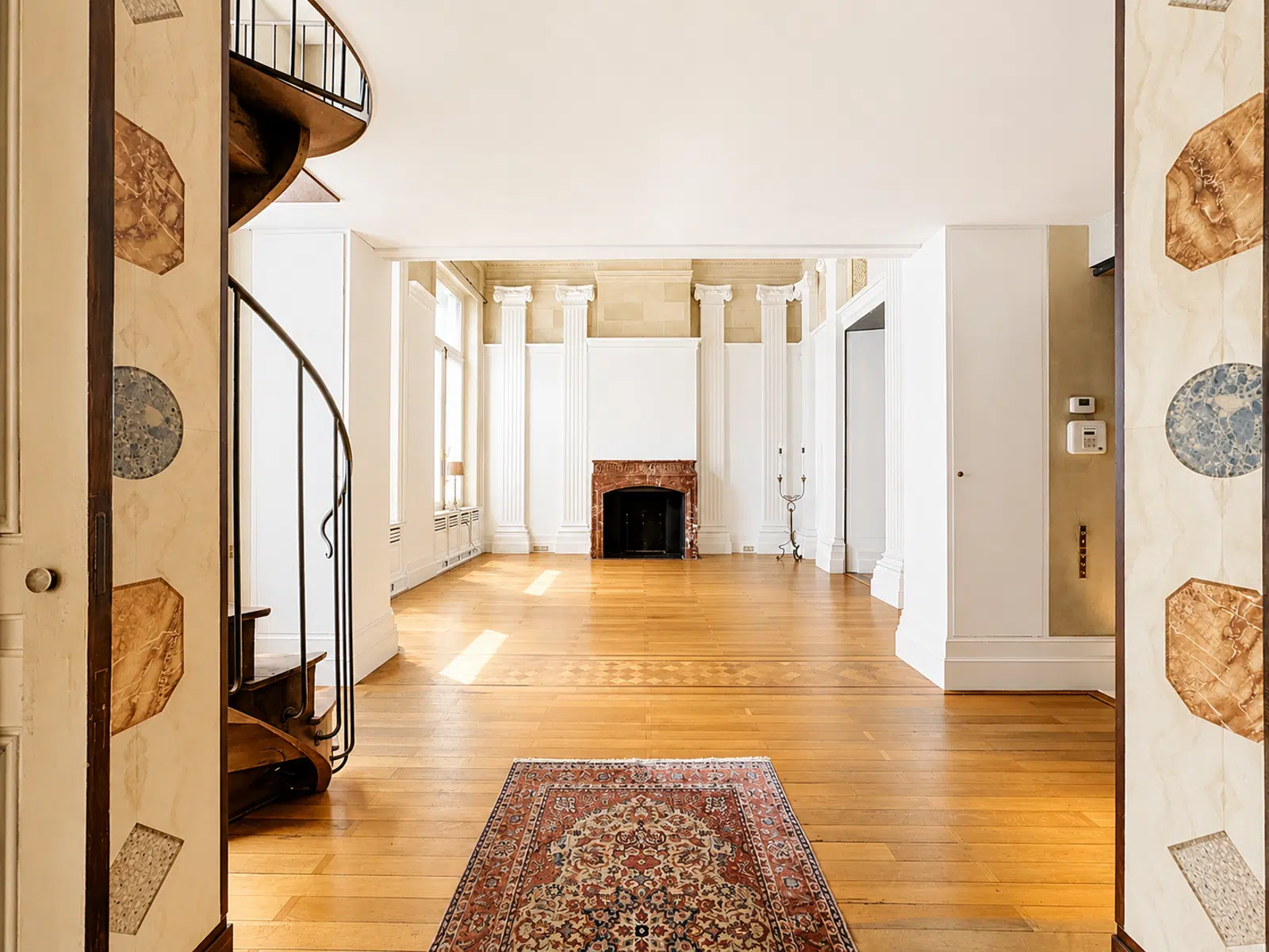 whise photo 2 Elegant empty living room with a marble fireplace, tall white columns, and a spiral staircase on the left.