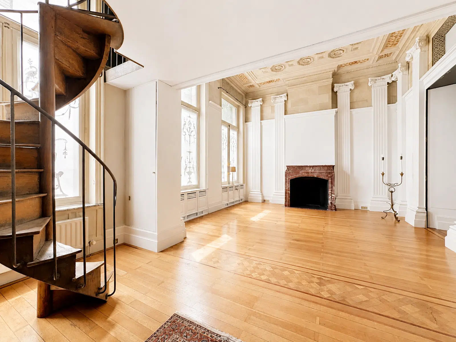 whise photo 6 Spiral wooden staircase on the left in a bright neoclassical living room with tall white columns and a marble fireplace.