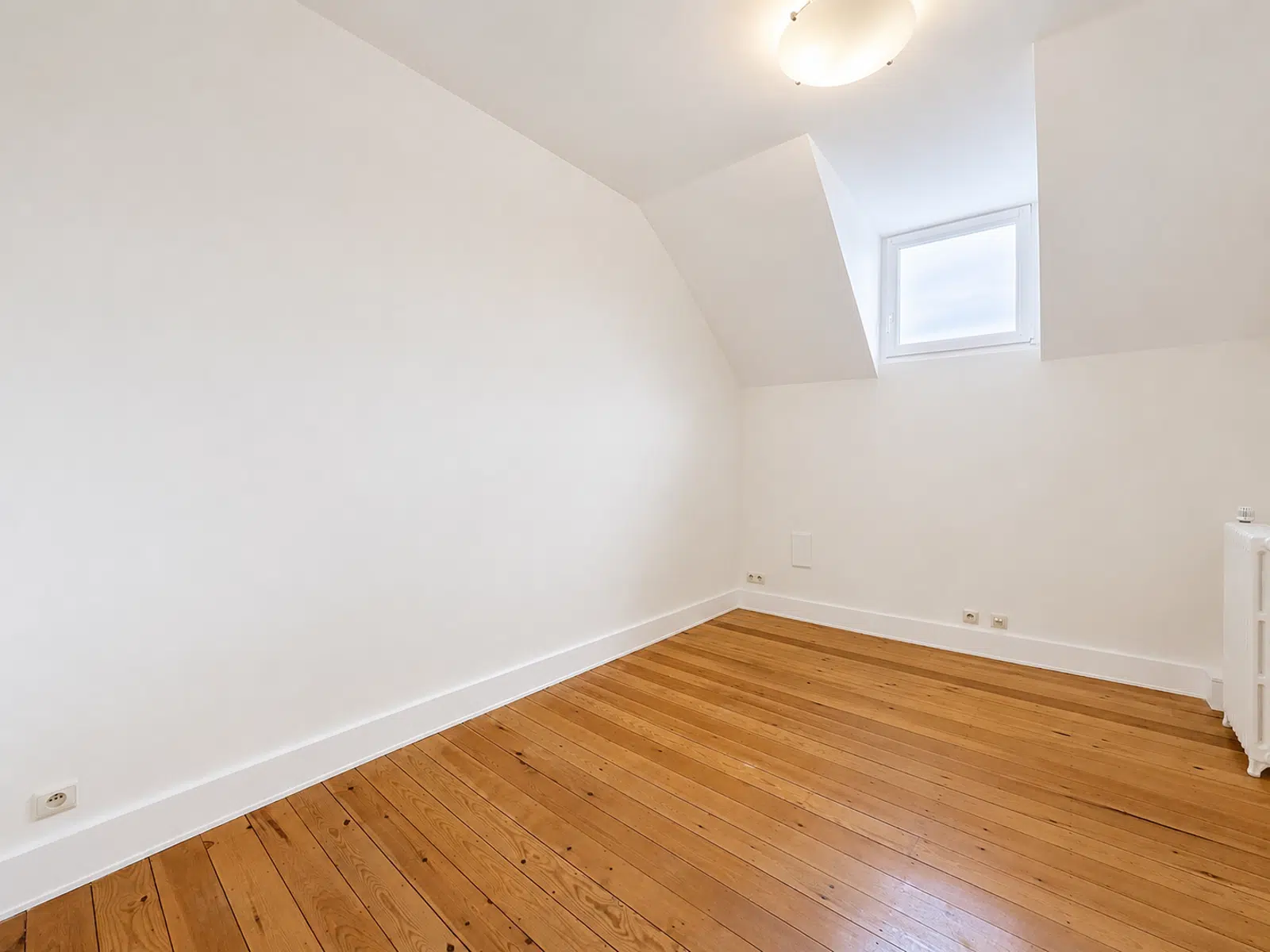 Pièce Mansardée Lumineuse – You Real Estate Agency Pièce mansardée lumineuse avec parquet en bois dans appartement rénové.