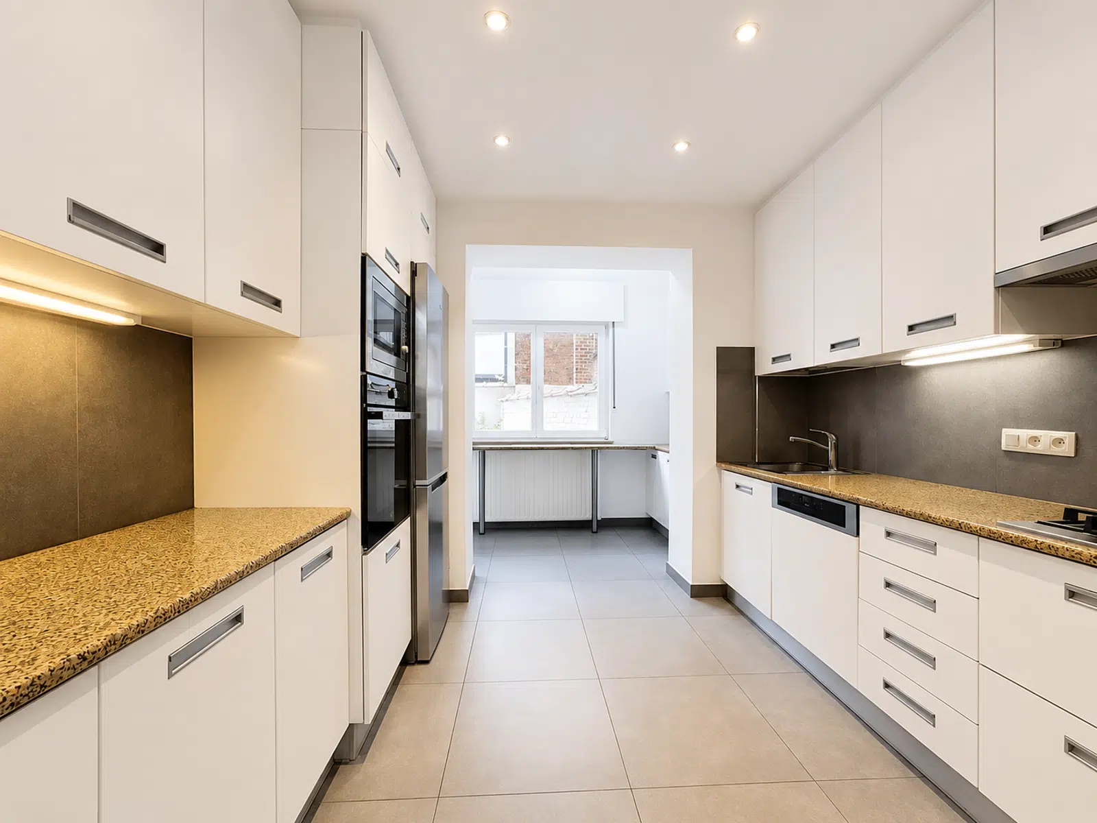 Cuisine Équipée Moderne et Lumineuse – You Real Estate Agency Cuisine équipée moderne d’appartement avec rangements blancs et coin repas lumineux.