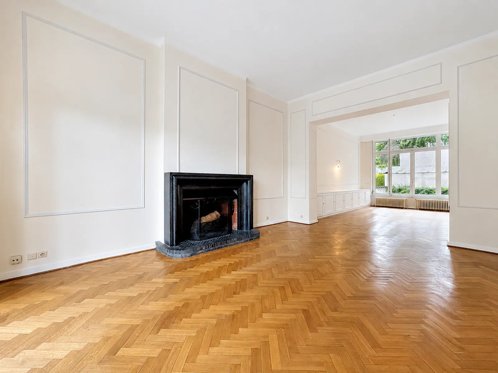 Salon Élégant avec Cheminée et Parquet – You Real Estate Agency Salon élégant avec parquet en chevrons, cheminée noire et moulures dans appartement ancien.