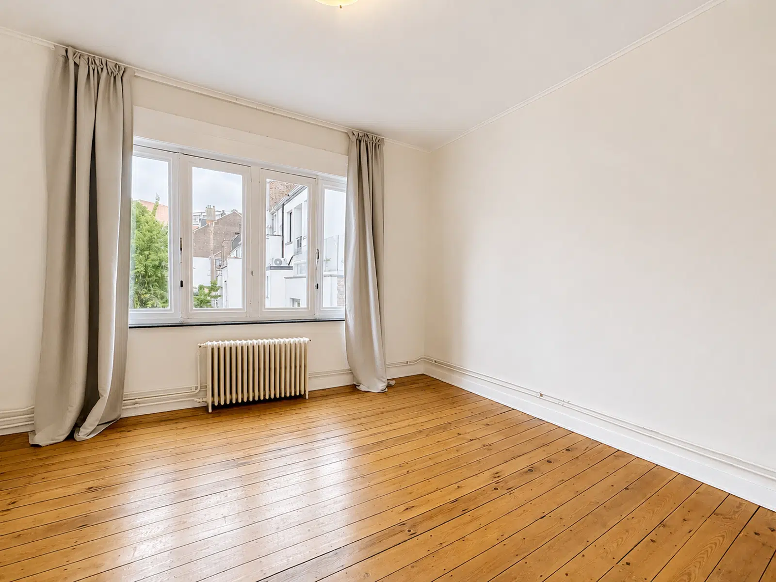 Salon Lumineux avec Parquet – You Real Estate Agency Salon lumineux d’appartement vide avec parquet, grande fenêtre et radiateur.