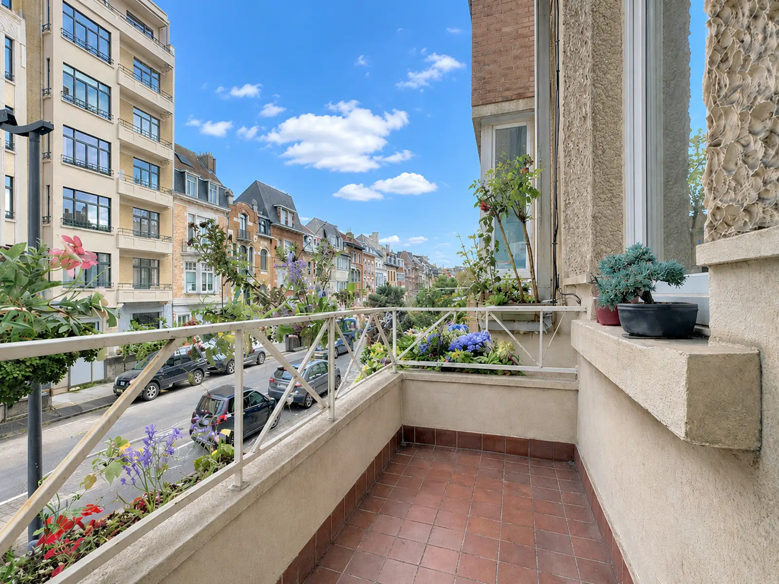 Flowered Balcony with Residential View - You Real Estate Agency Flower-filled balcony overlooking residential street and elegant facades.