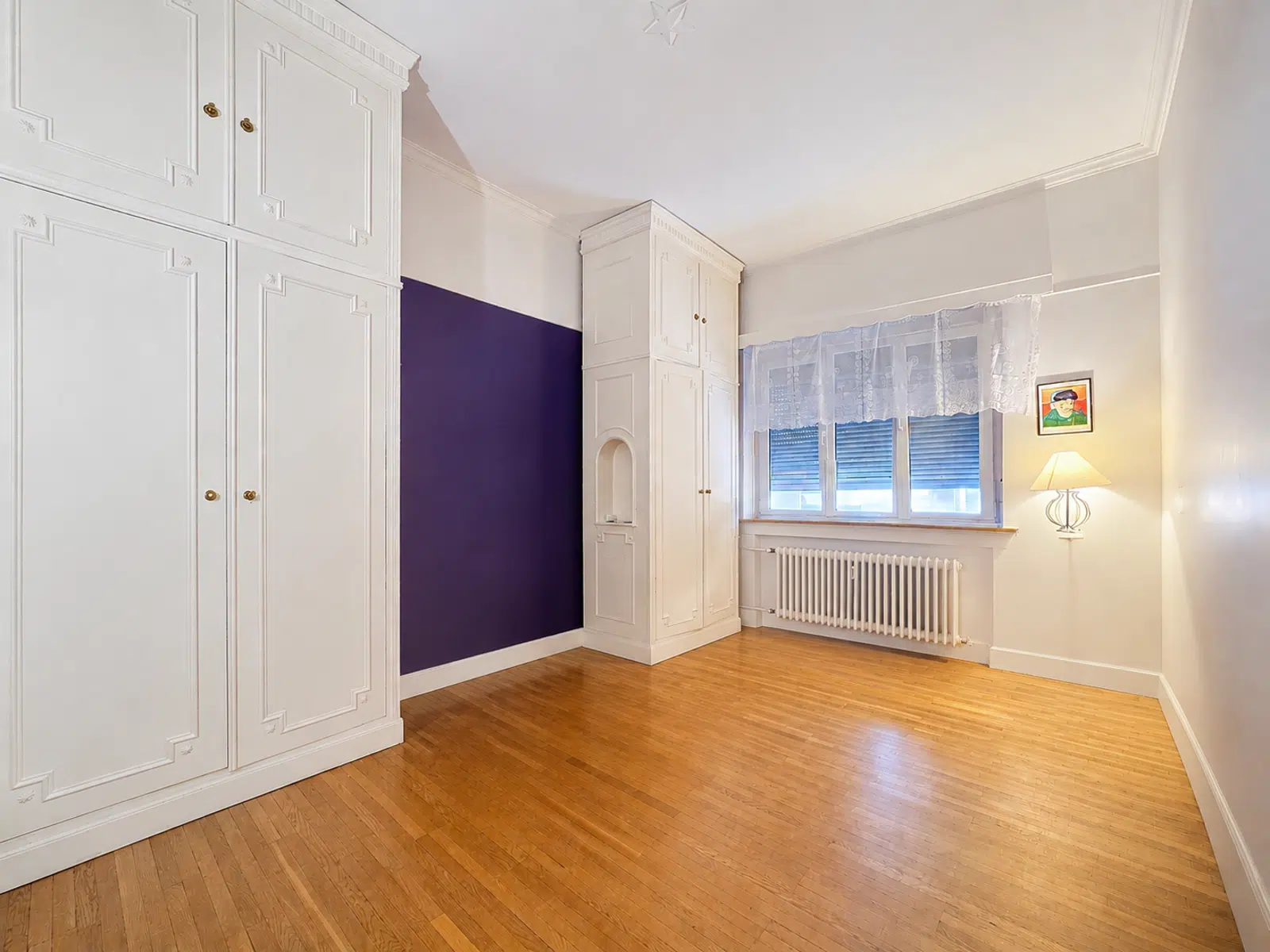 Bright bedroom with fitted closets - You Real Estate Agency Bright bedroom with parquet floor, built-in closets and purple wall in apartment.
