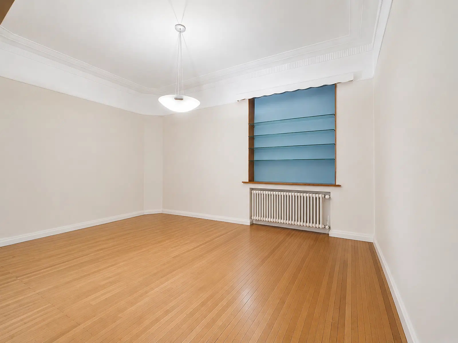 Bright living room with parquet floor - You Real Estate Agency Empty apartment living room with wooden floor, moldings, window and radiator.