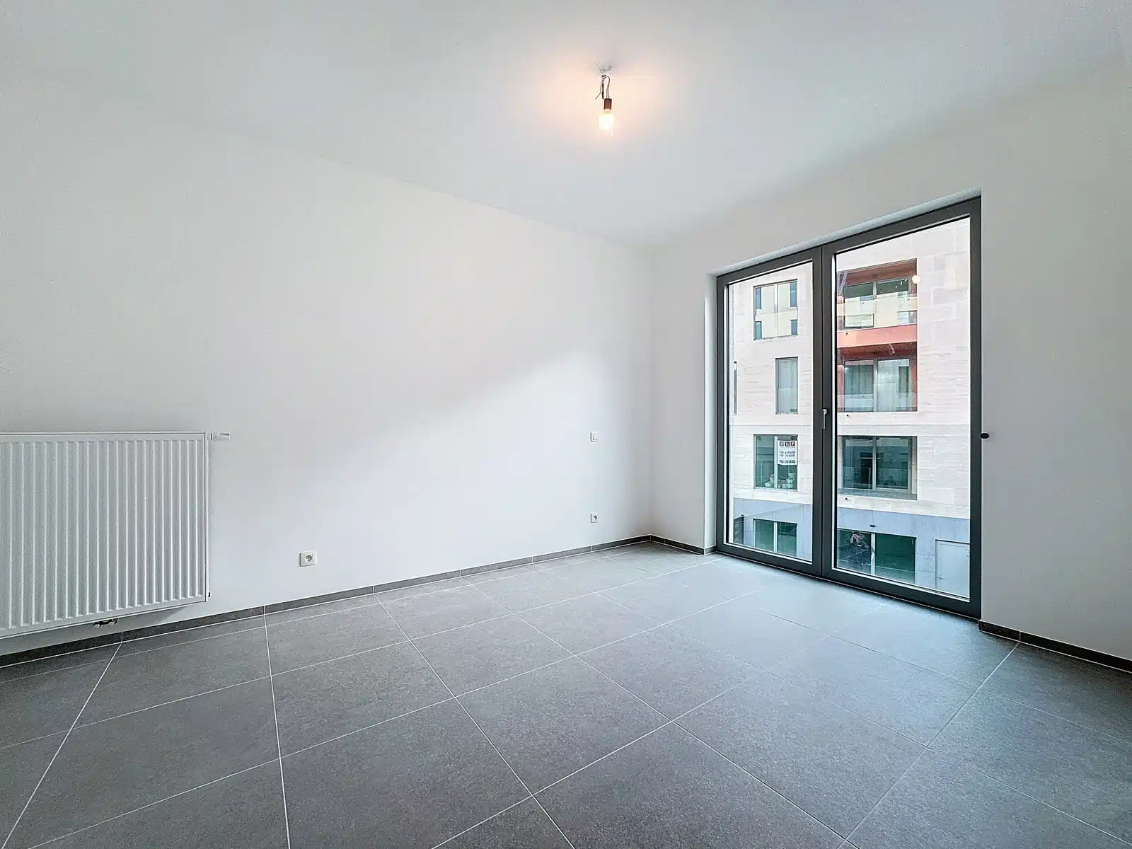 Lichte kamer met erker - Uw Makelaarskantoor Lichte kamer in een moderne flat met erker en grijze tegelvloer.
