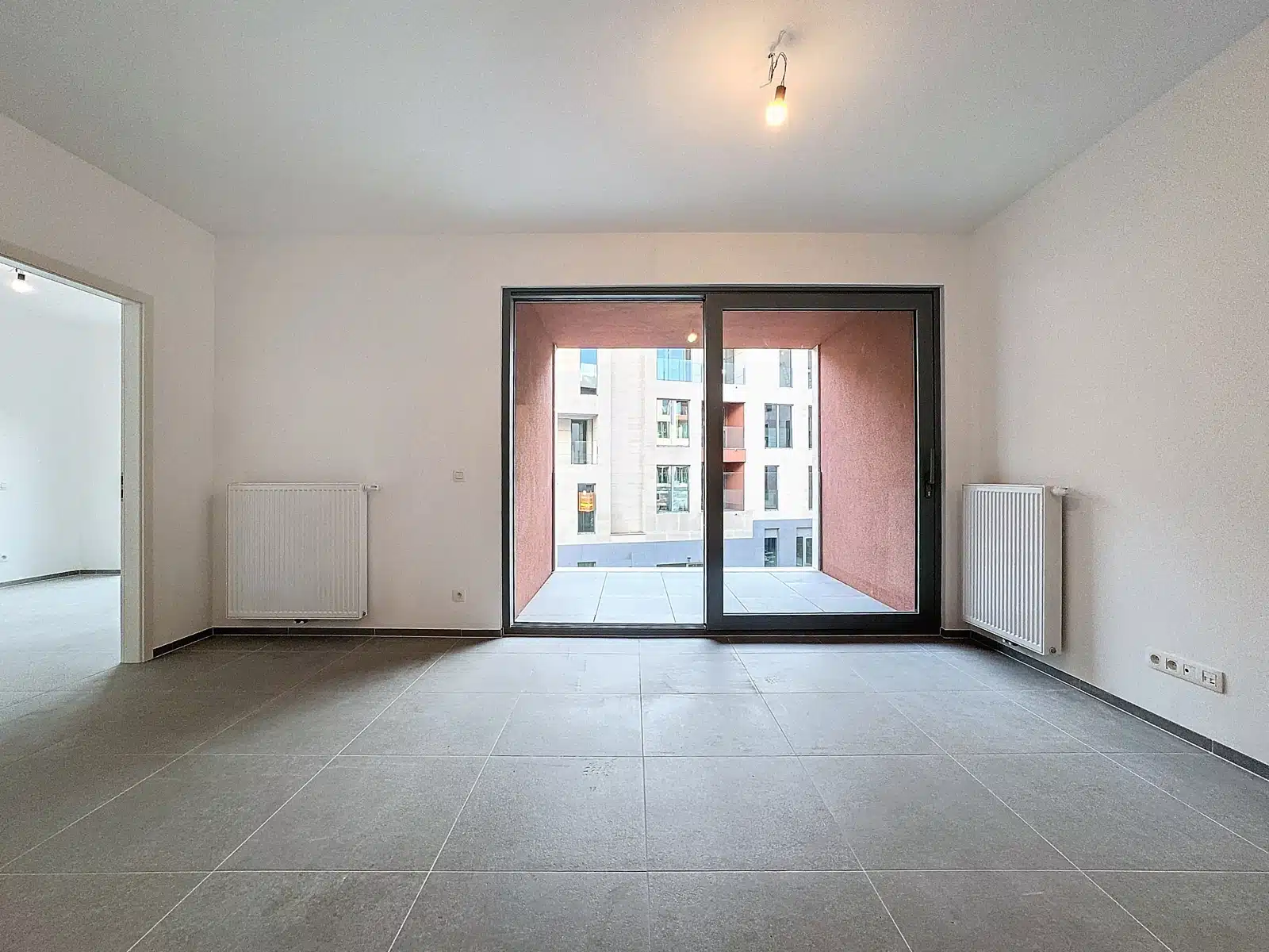 Lichte woonkamer met terras - You Real Estate Agency Lege woonkamer in een moderne flat met overdekt terras en grijze tegelvloer.