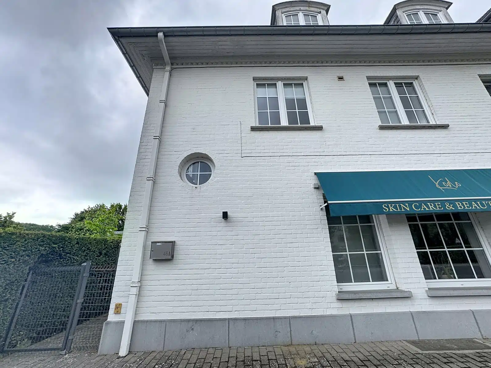 whise photo 11 White brick building with a teal storefront awning reading 'Skin Care & Beauty' over large shop windows. Cloudy sky above.