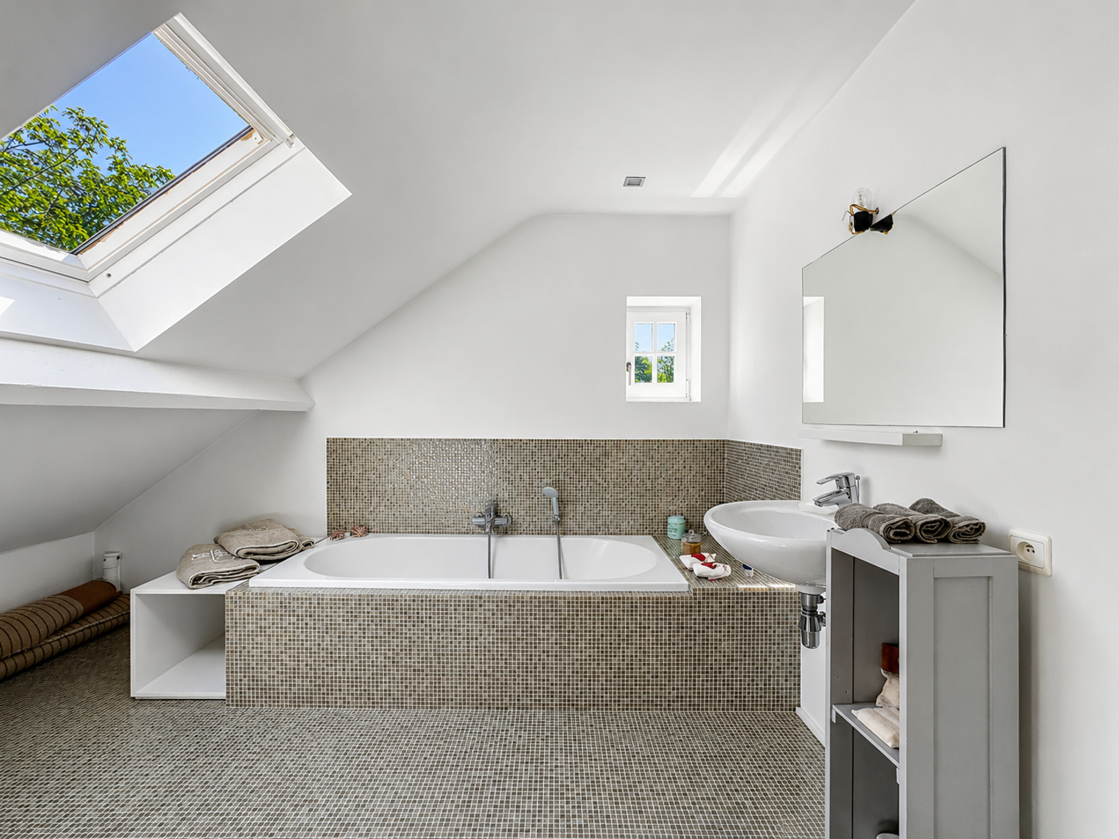 Salle de Bain Mansardée Lumineuse – You Real Estate Agency Salle de bain mansardée avec baignoire encastrée et puits de lumière dans maison moderne.