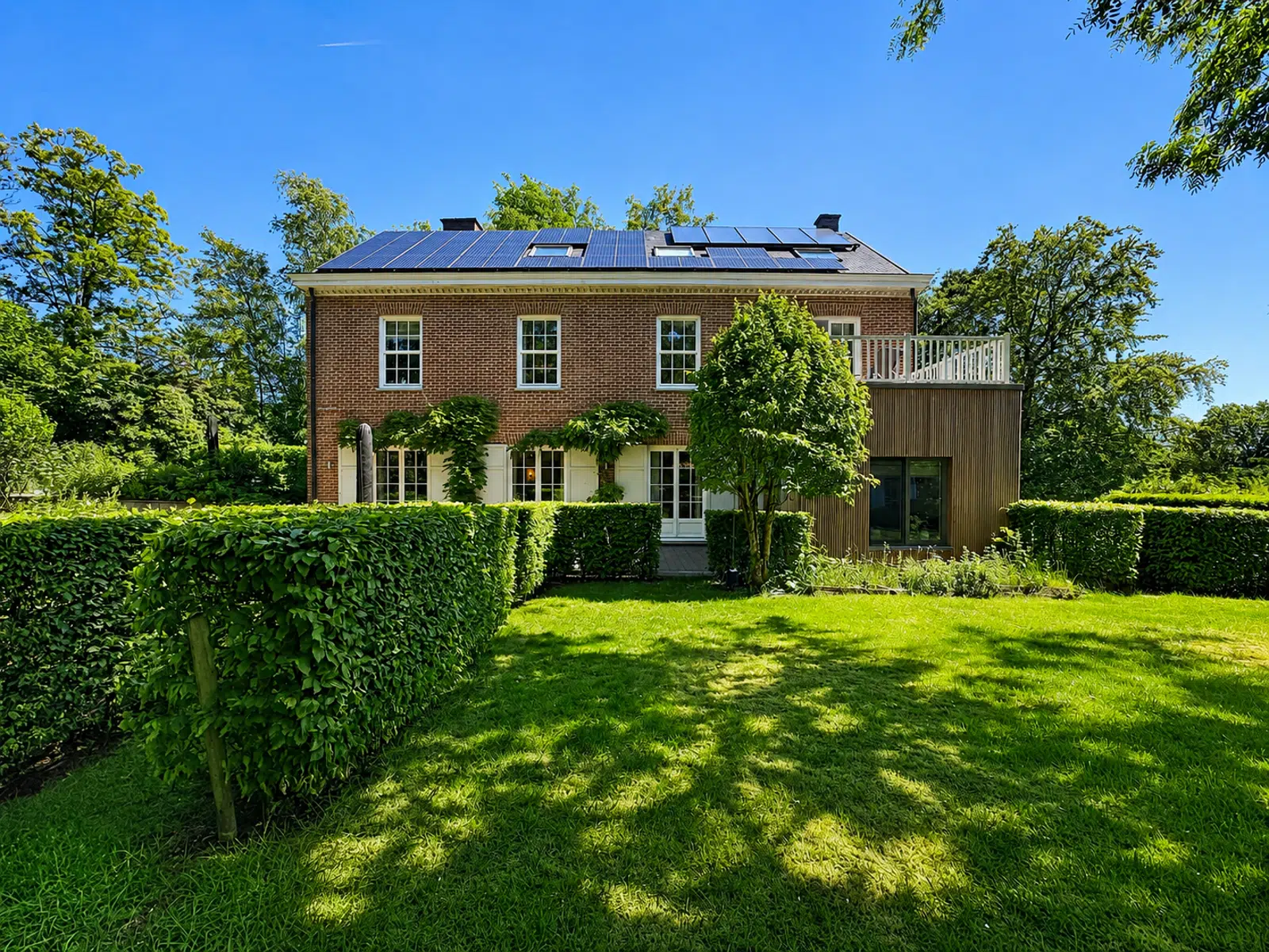 Façade Arrière Avec Jardin – You Real Estate Agency Maison en brique avec terrasse, panneaux solaires et grand jardin paysager.