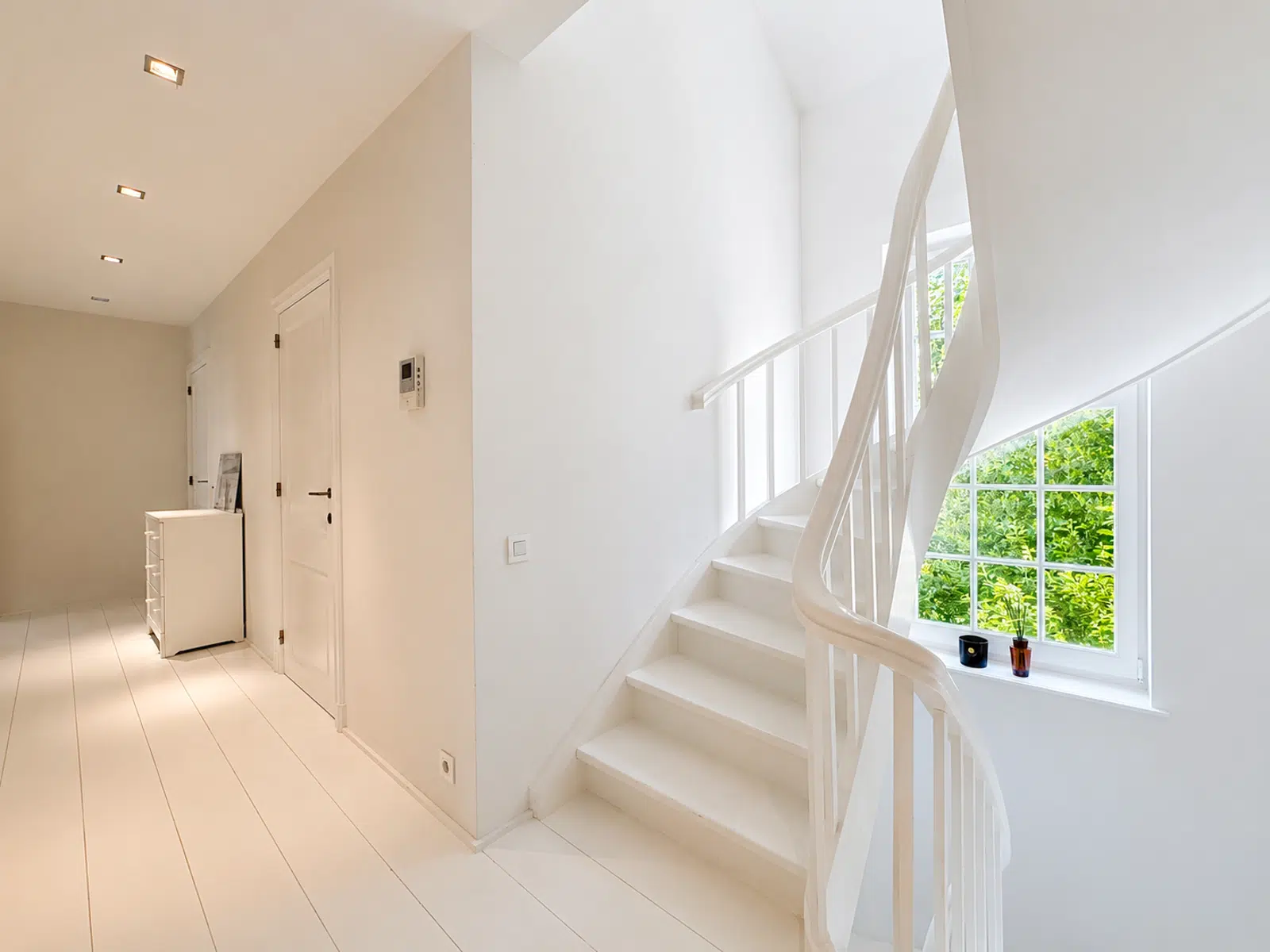 Hall Lumineux avec Escalier Blanc – You Real Estate Agency Hall d’entrée lumineux avec escalier blanc et grande fenêtre dans une maison moderne.