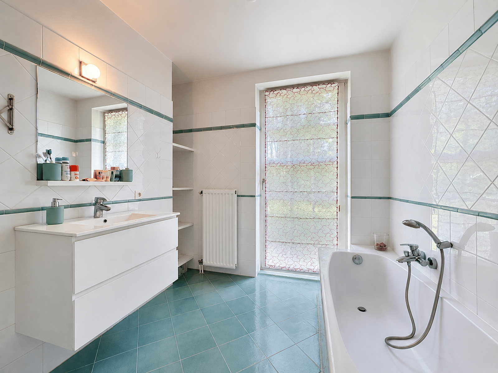 Salle de Bain Lumineuse – You Real Estate Agency Salle de bain lumineuse avec baignoire, meuble vasque blanc et carrelage turquoise en appartement.