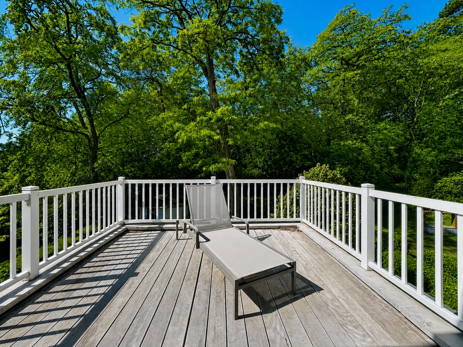 Terrasse en Bois avec Transat – You Real Estate Agency Terrasse en bois avec transat, garde-corps blanc et vue sur jardin arboré.