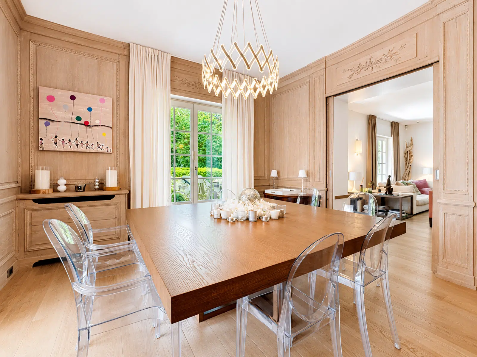 Salle à Manger Élégante – You Real Estate Agency Salle à manger élégante de maison avec table en bois, lustre design et terrasse.