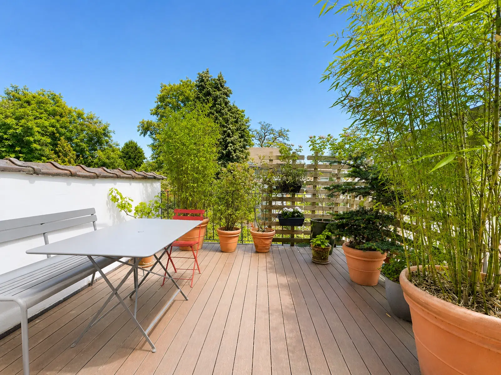 Terrasse en Bois Ensoleillée – You Real Estate Agency Terrasse en bois ensoleillée avec mobilier de jardin et plantes luxuriantes.