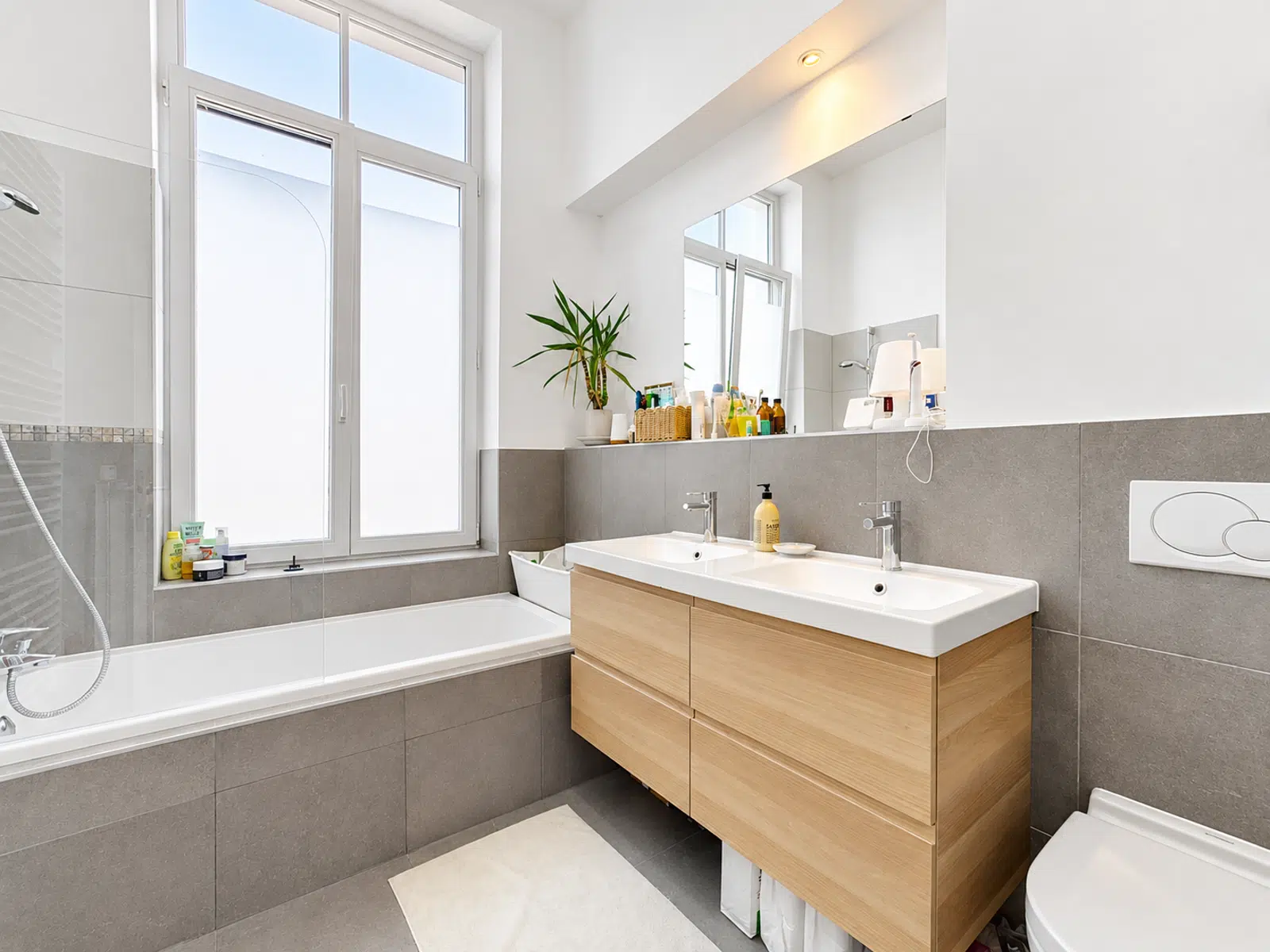 Salle de Bain Moderne Lumineuse – You Real Estate Agency Salle de bain moderne avec baignoire, double vasque et grande fenêtre en appartement.
