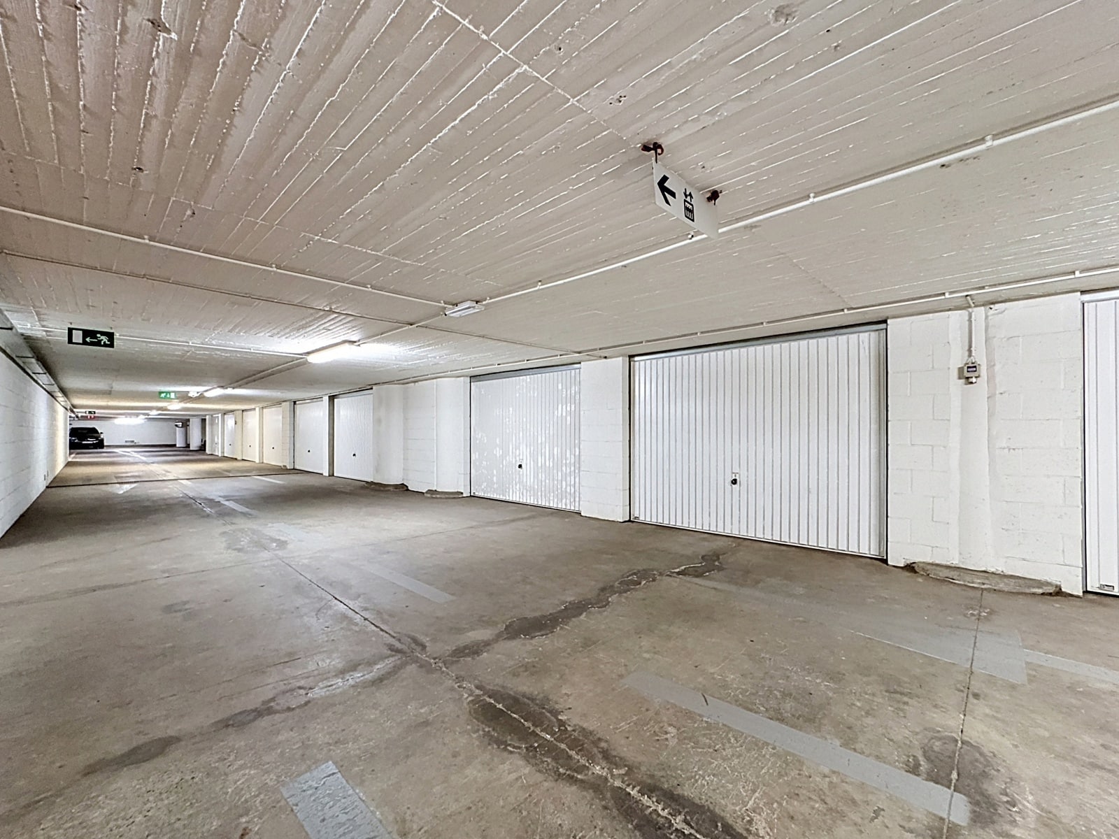 Garage Souterrain avec Boxes Privatifs – You Real Estate Agency Garage souterrain sécurisé avec boxes privatifs blancs et couloir éclairé.