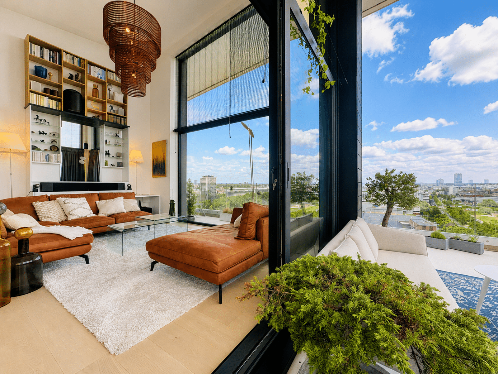 whise photo 2 Living room with orange sectional sofa, white rug, and wall shelves, opening to a balcony with a city skyline through large glass doors.