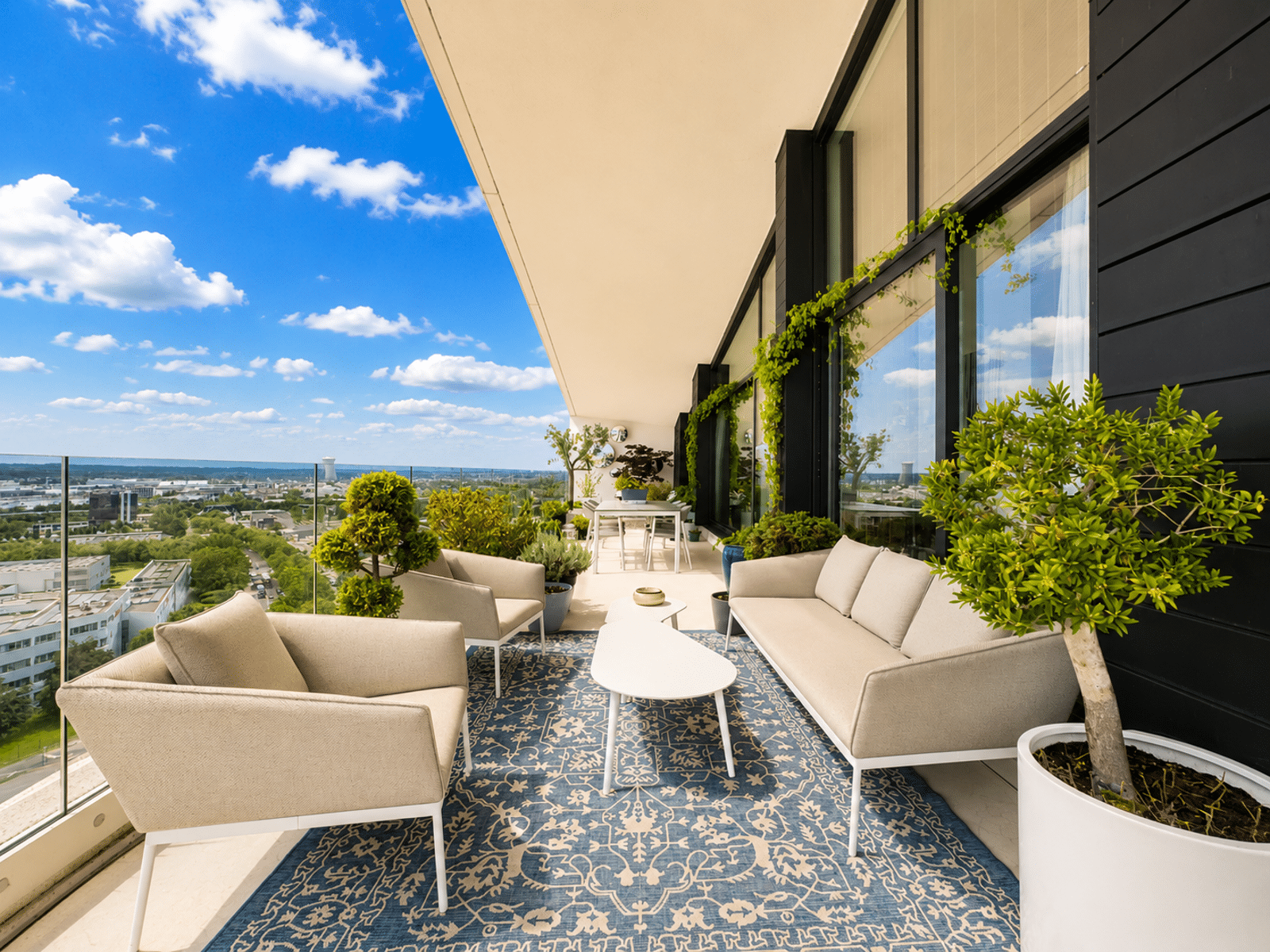 Terrasse Moderne Avec Vue Urbaine – You Real Estate Agency Terrasse d’appartement moderne avec salon extérieur, végétation et vue panoramique urbaine.