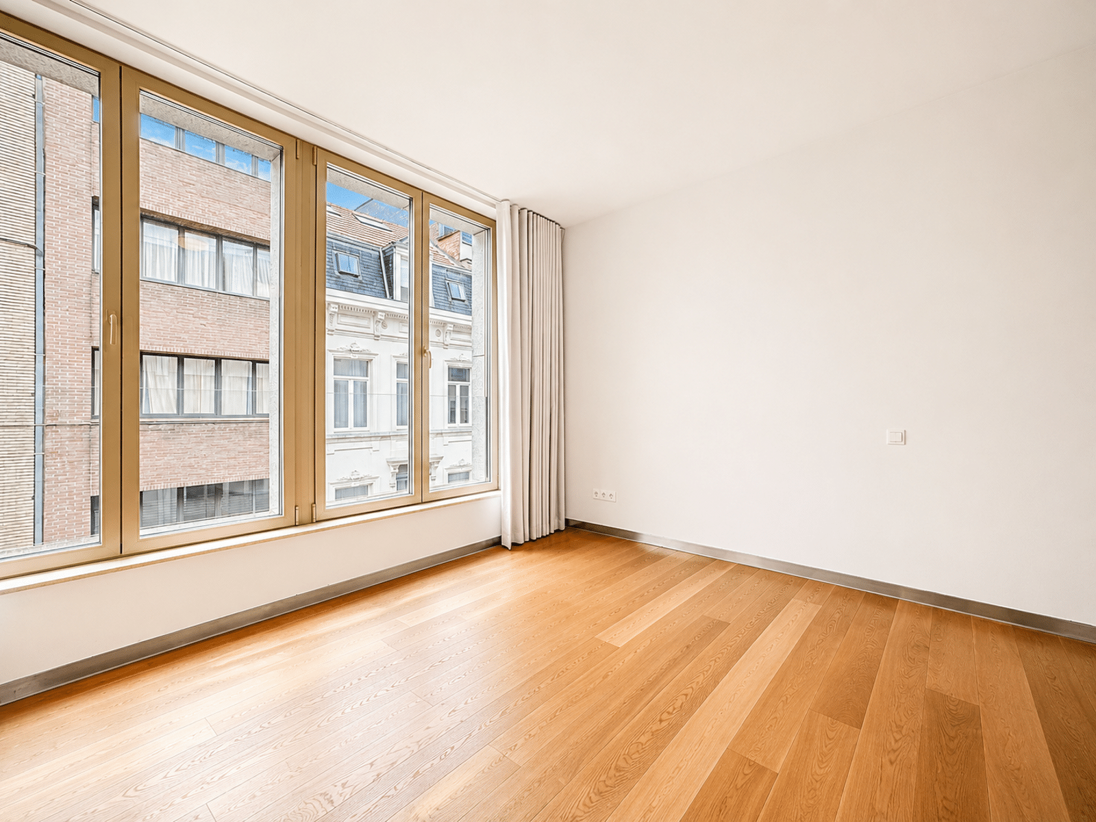 Pièce Lumineuse à Grandes Fenêtres – You Real Estate Agency Pièce lumineuse d’appartement avec parquet, grandes fenêtres et vue urbaine.