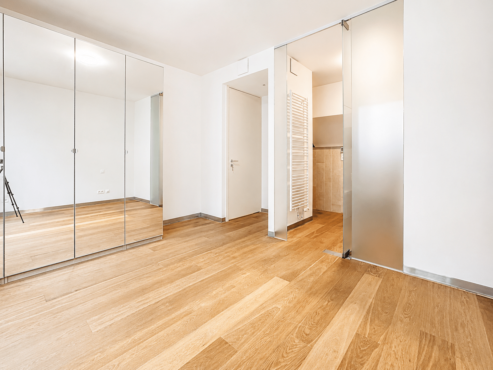 Chambre Moderne avec Placards Miroirs – You Real Estate Agency Chambre d’appartement lumineuse avec placards miroirs, parquet clair et accès salle d’eau.
