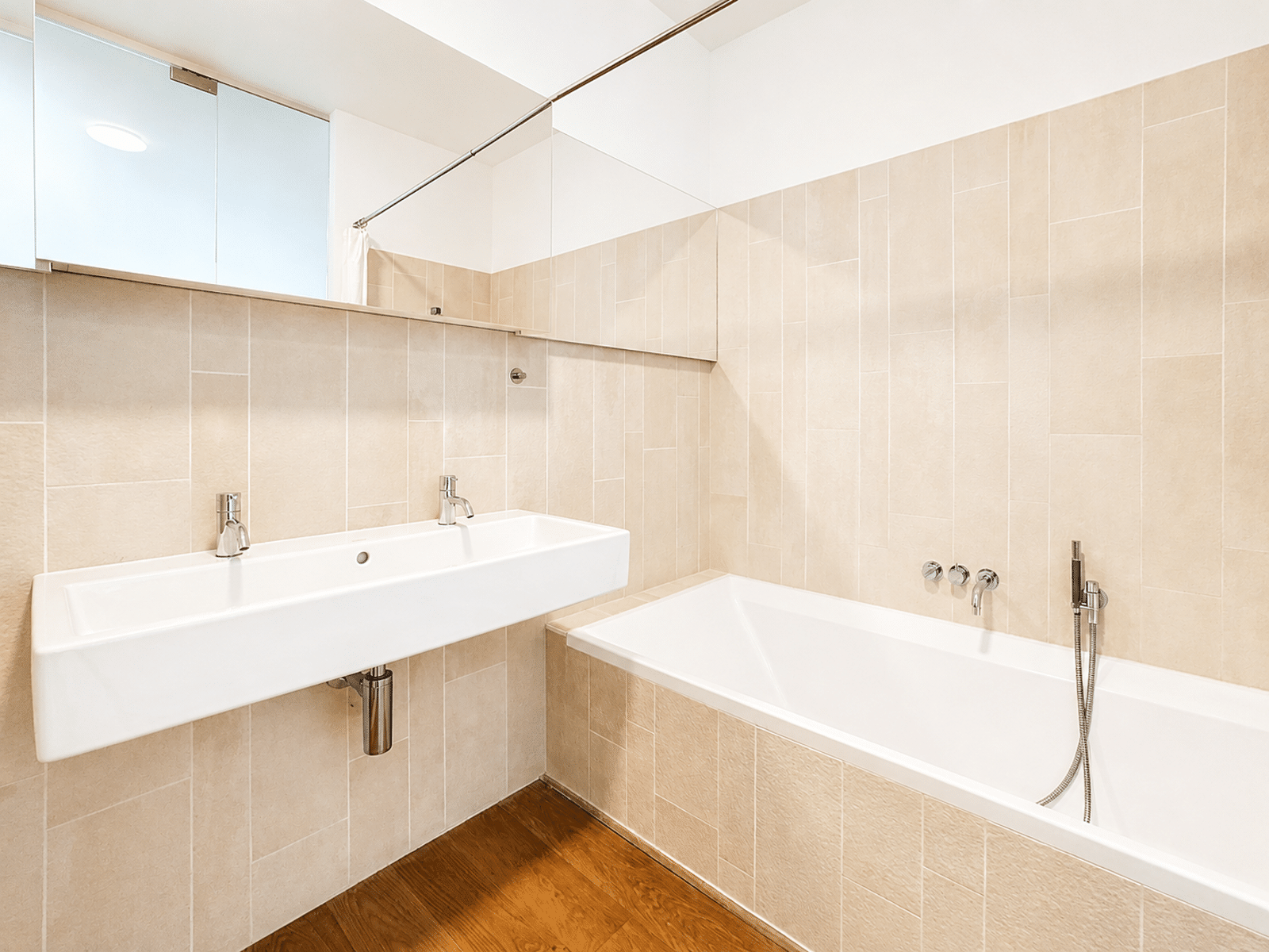 Salle de Bain Moderne avec Baignoire – You Real Estate Agency Salle de bain moderne d’appartement avec double vasque, baignoire et carrelage beige.