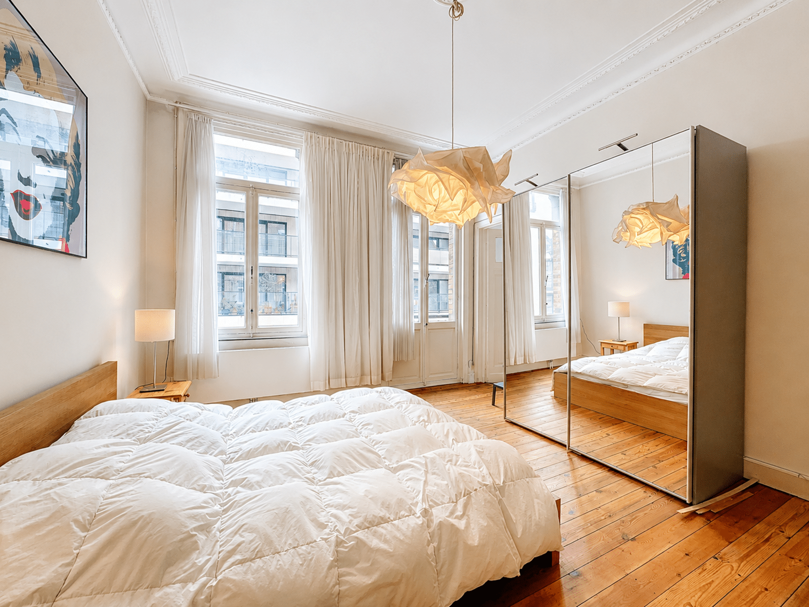 Wijze foto 9 Lichte, moderne slaapkamer met wit gewatteerd bed, houten vloeren en een grote spiegelkast.