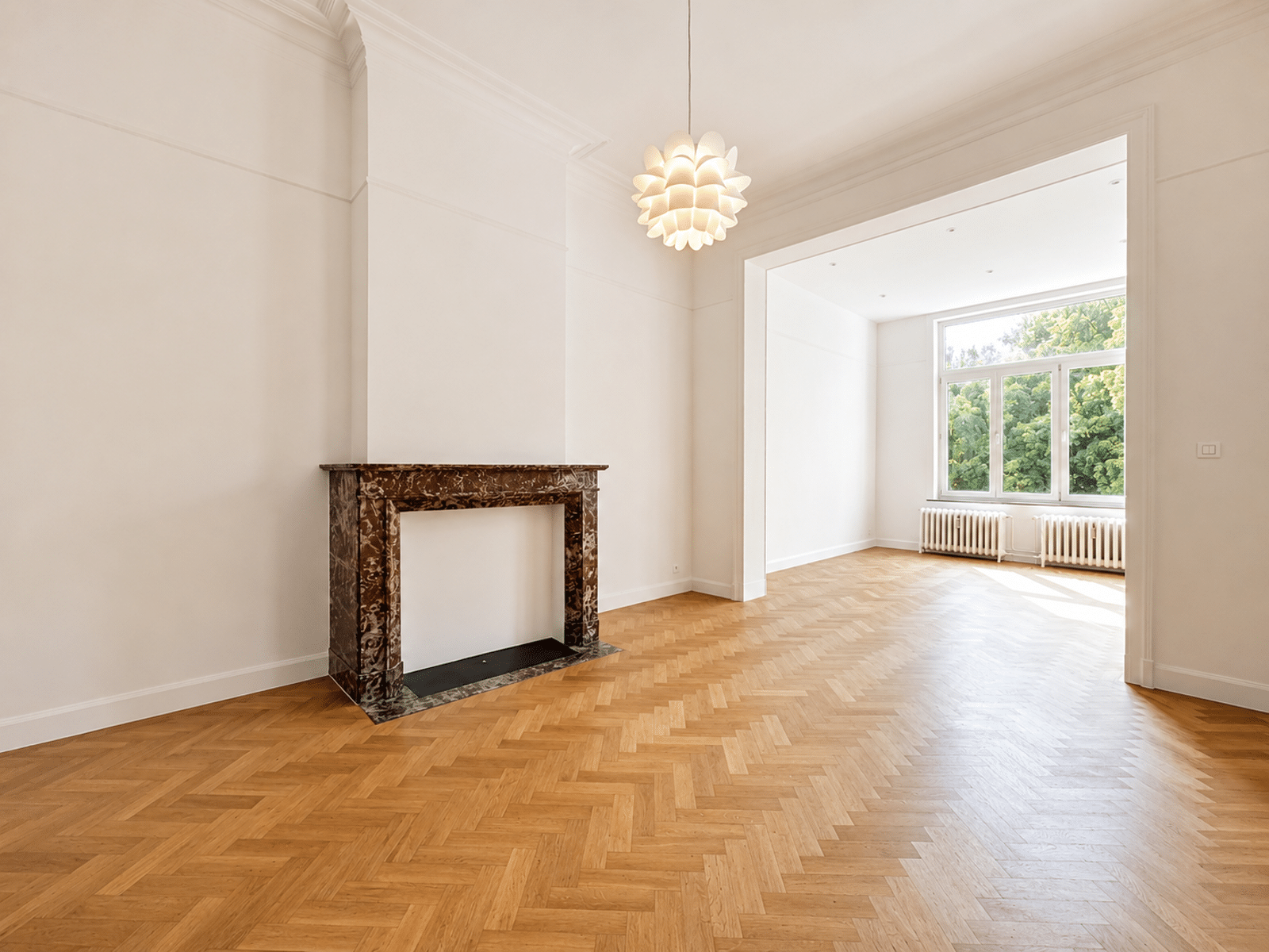 Bright living room with fireplace - You Real Estate Agency Bright, empty living room with herringbone wood floor, marble fireplace, and large window letting in daylight