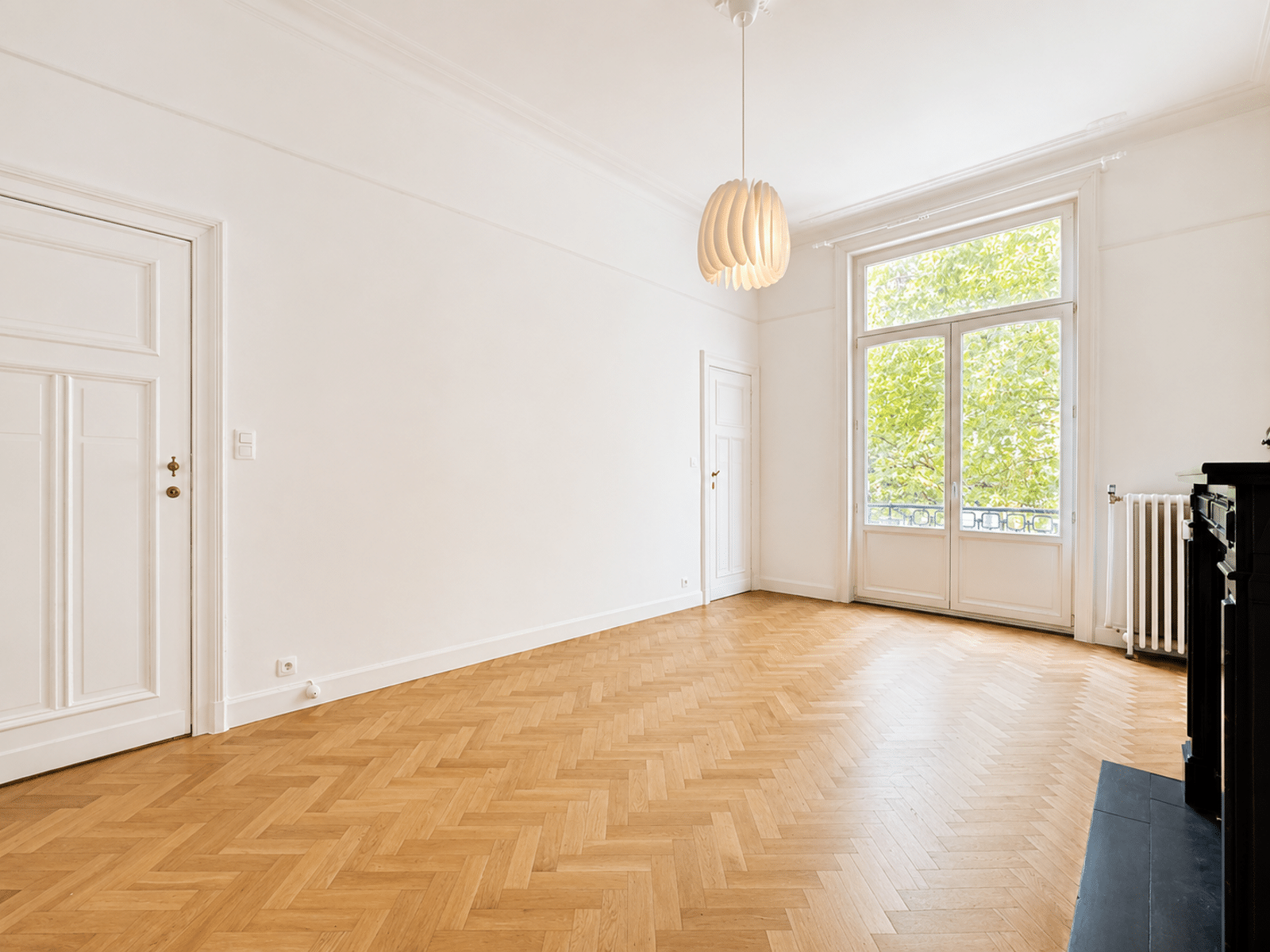 Bright living room with balcony - You Real Estate Agency Salon d’appartement lumineux avec parquet en point de Hongrie et balcon.