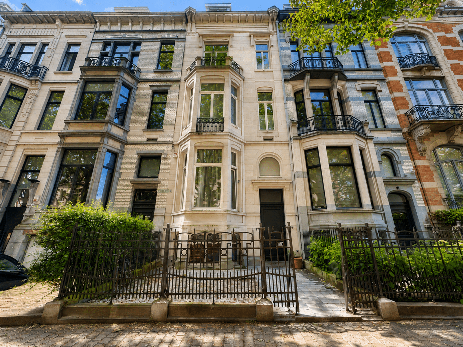 Façades de Maisons de Ville – You Real Estate Agency Maisons de ville élégantes avec façades historiques et balcons dans quartier résidentiel arboré.