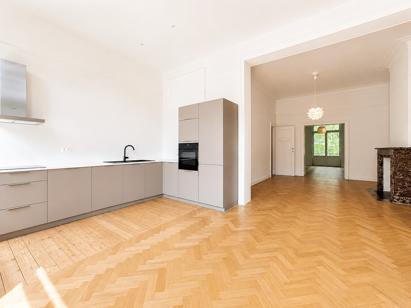 whise photo 5 Open-plan kitchen with light gray flat-panel cabinets, built-in oven, black sink faucet, and herringbone wood floor.