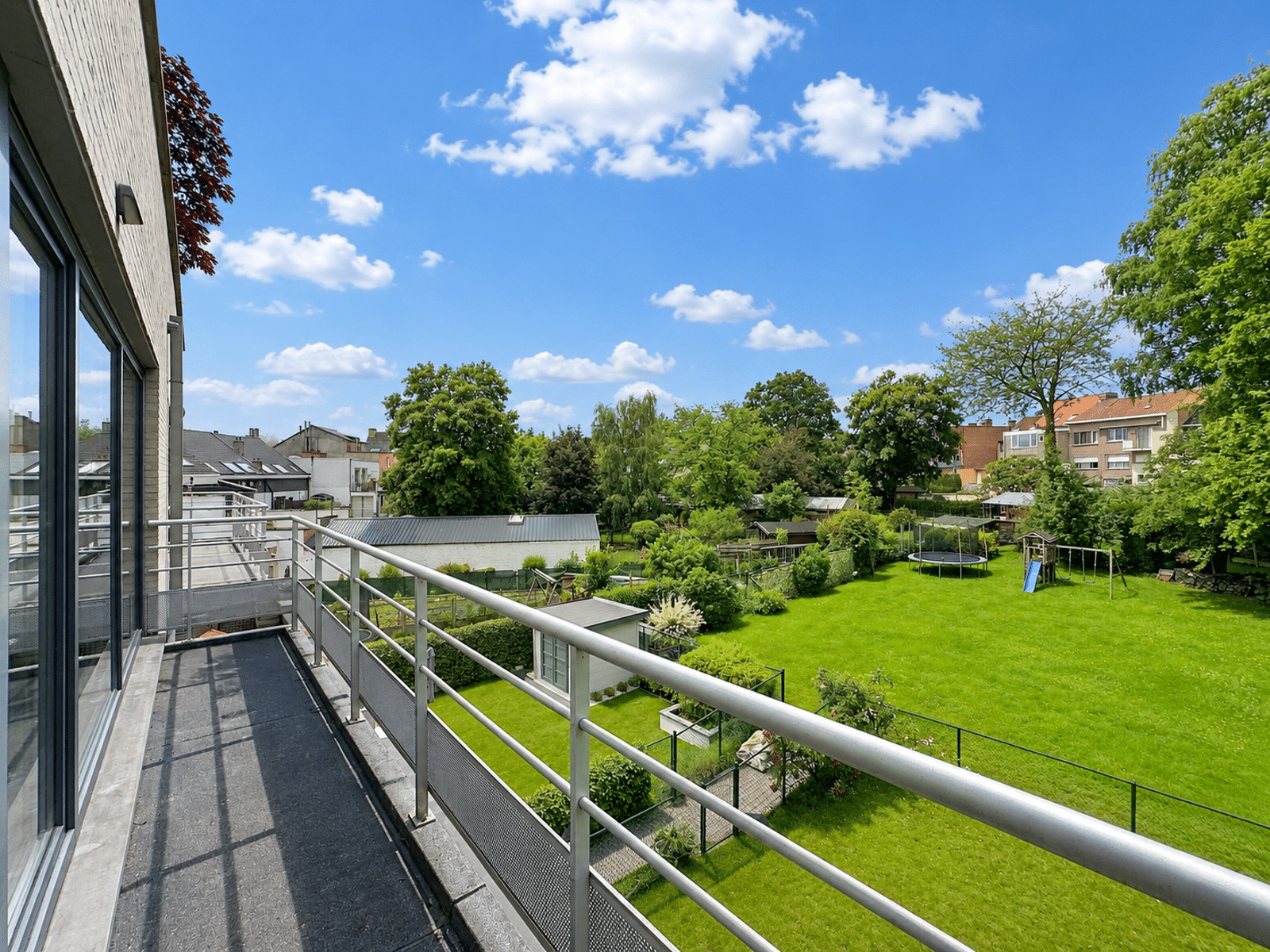 whise photo 3 Balcony view overlooking a sunny green backyard with a trampoline and slide, surrounded by trees and neighboring houses.