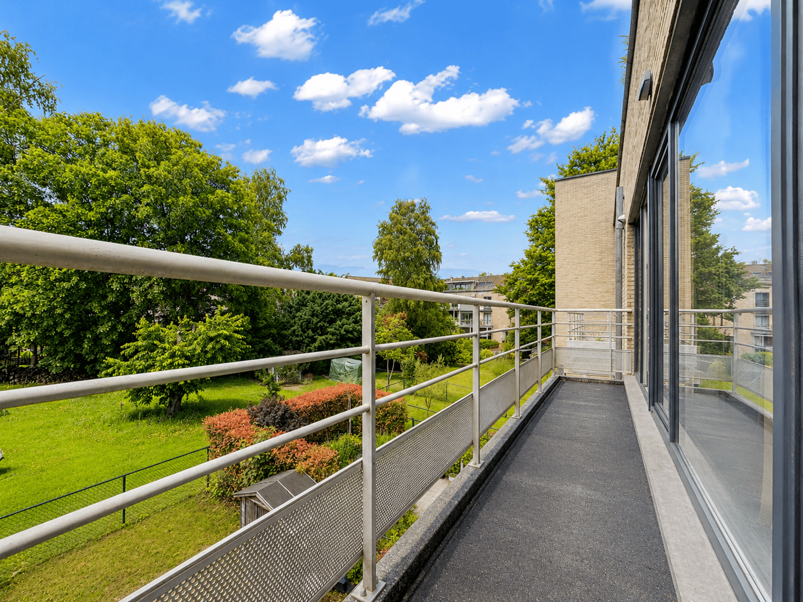 Modern balcony with garden view - You Real Estate Agency Modern apartment terrace overlooking green garden.