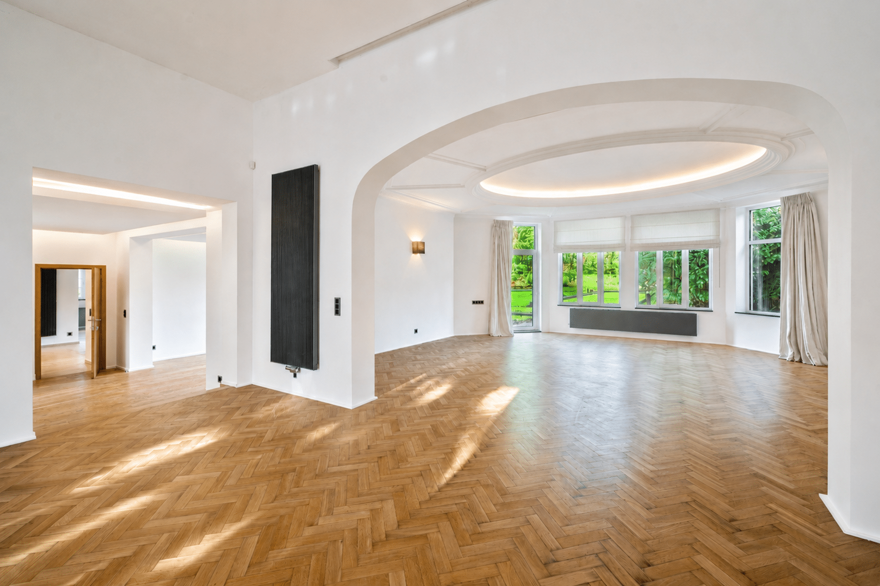 Lichte woonkamer met parketvloer - You Real Estate Agency Lichte, lege vlakke woonkamer met visgraat parketvloer en grote ramen.