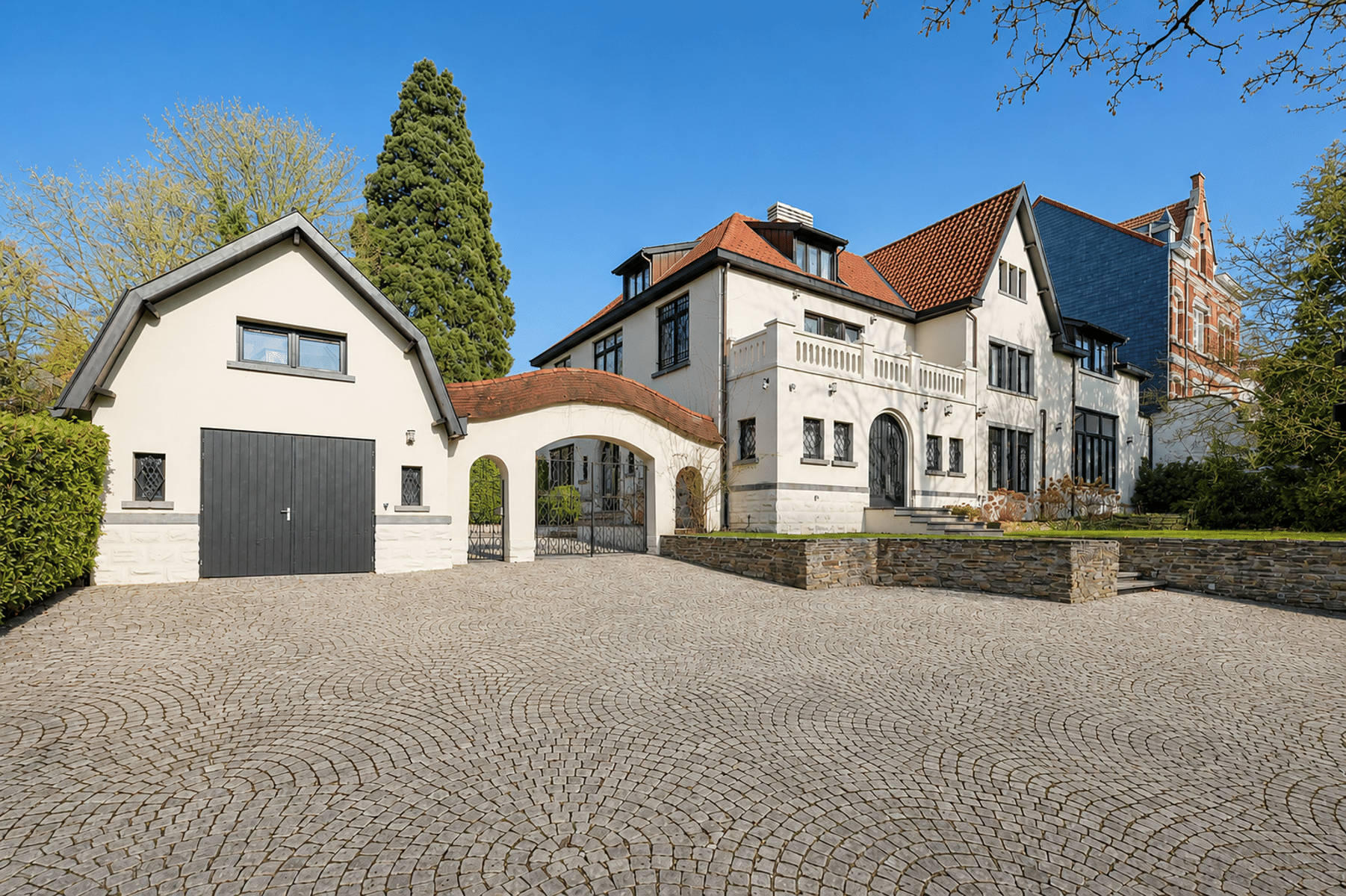 Prestige Villa gevel - U Vastgoedkantoor Prestigieus huis met geplaveide binnenplaats, garage en rood pannendak.