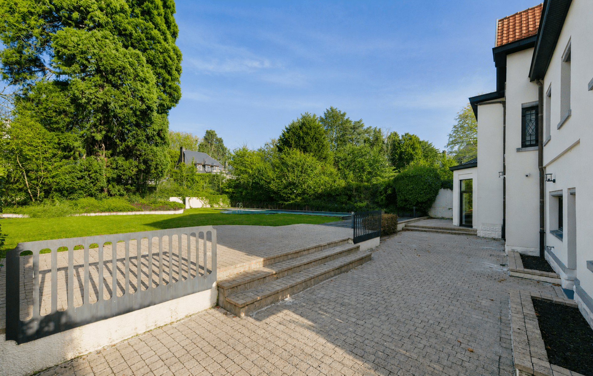 Betegeld terras met zwembad - You Real Estate Agency Wit huis met groot betegeld terras, zwembad en beboste tuin.