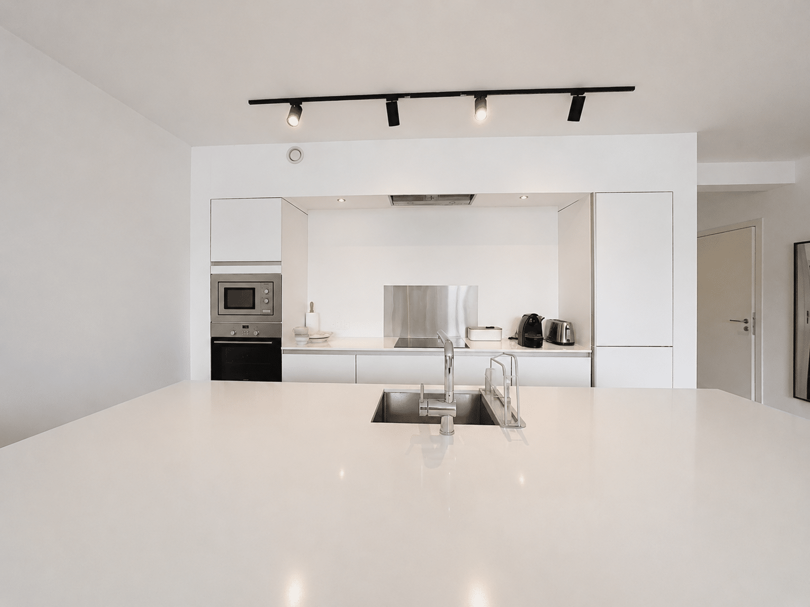 Cuisine Blanche avec Îlot – You Real Estate Agency Cuisine moderne blanche avec îlot central et électroménager intégré dans appartement contemporain.