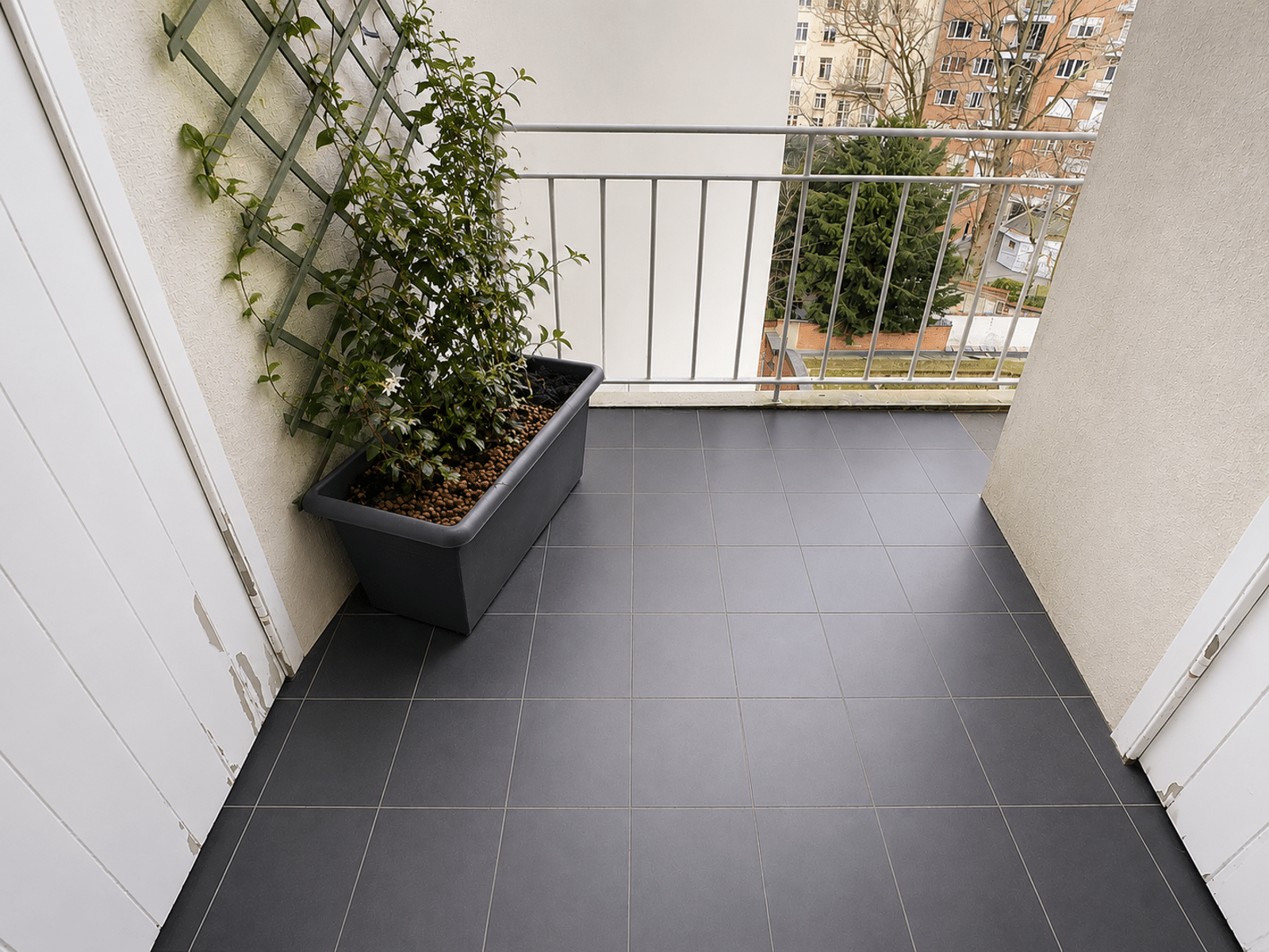 whise photo 8 Balcony with a rectangular planter of pebbles and a climbing vine against a lattice, overlooking city buildings.