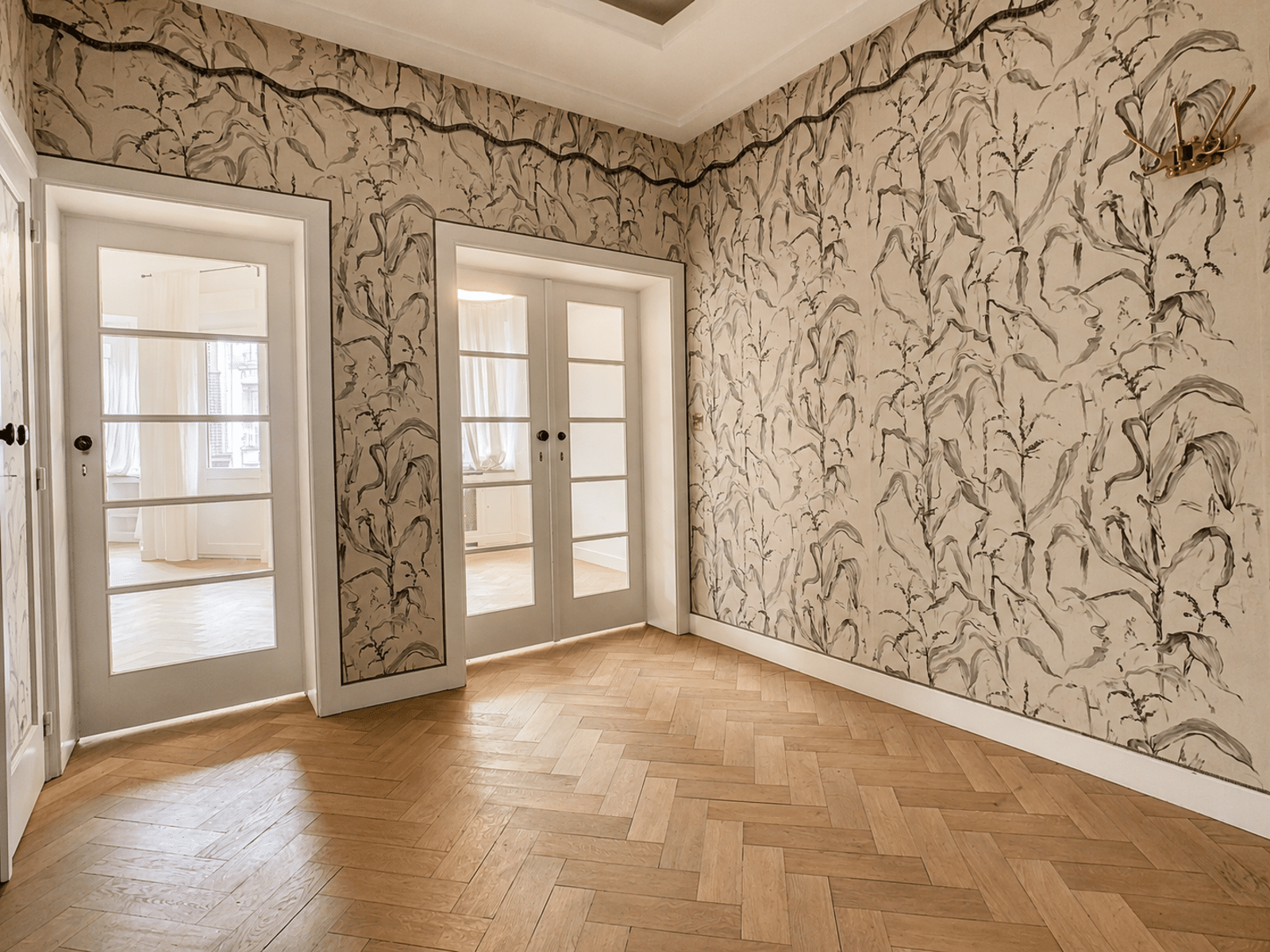 whise photo 9 Bright hallway with light wood herringbone floor, white walls, and a bold black-and-gray abstract botanical wallpaper; glass-paneled French doors on the left and center.