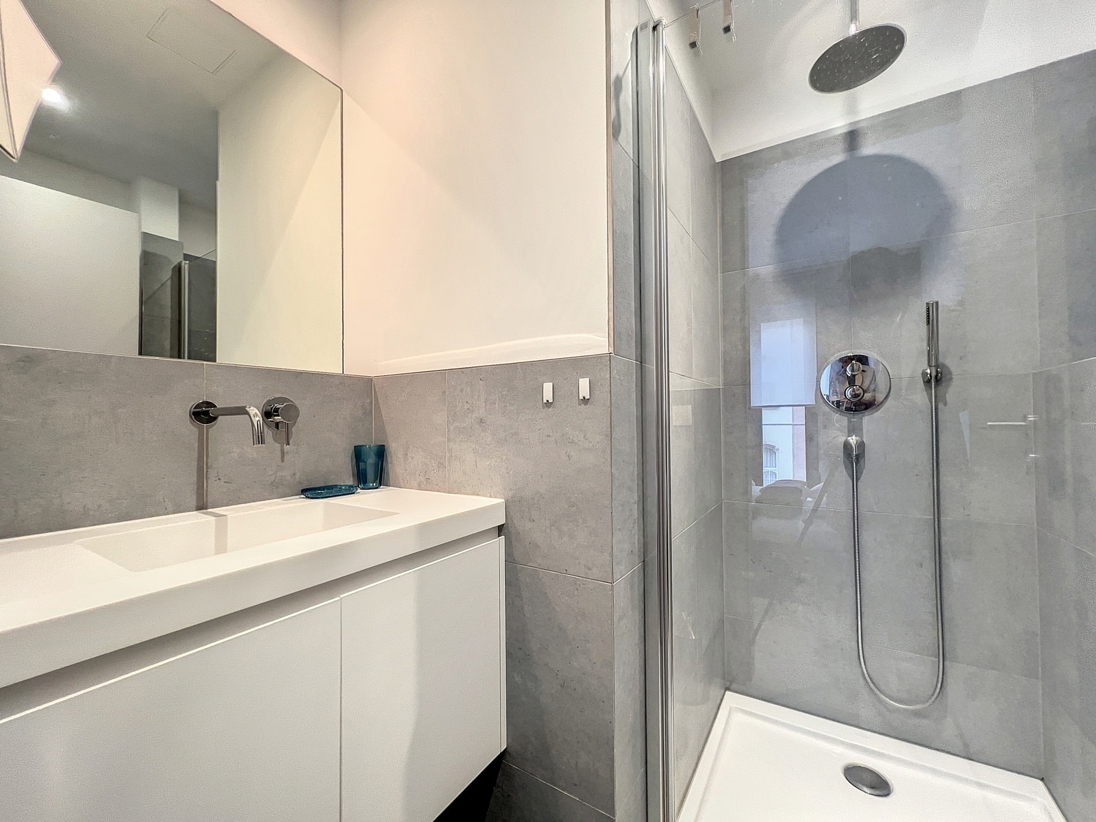 whise photo 5 Modern bathroom with a white vanity, wall-mounted faucet, large mirror, and a glass-enclosed shower with a rainfall showerhead.