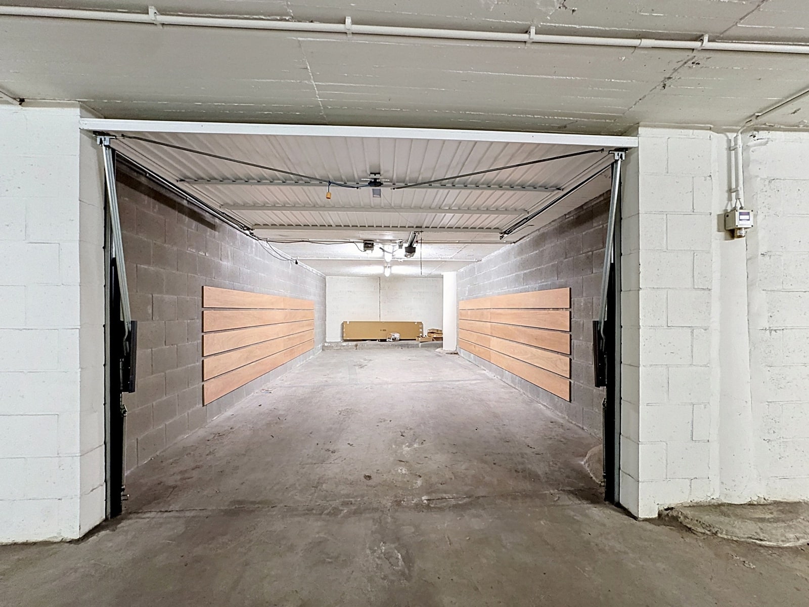 whise photo 2 Empty concrete garage with long wooden slat panels mounted on both side walls and a few boxes at the far end.