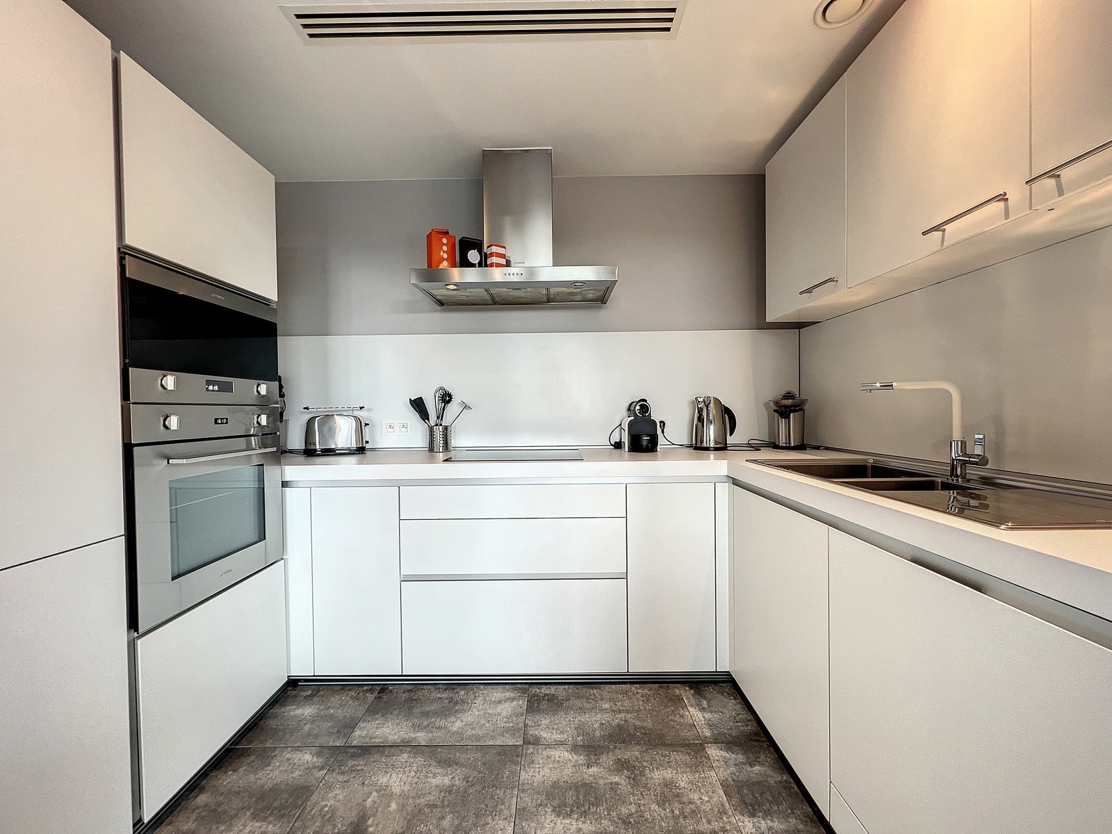 whise photo 4 Modern white kitchen with built-in double ovens, stainless range hood, and a slim counter with toaster and kettle.