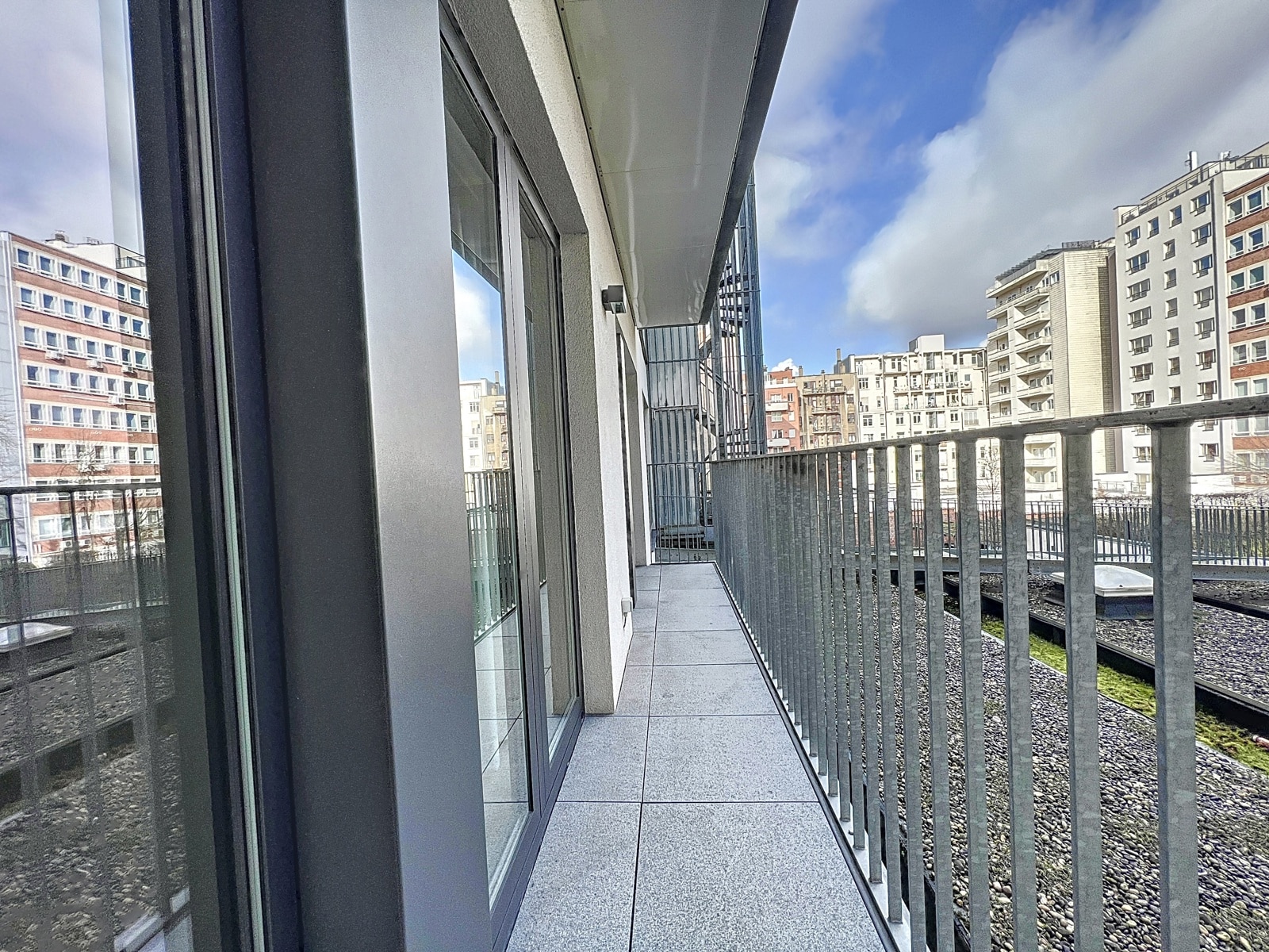 Balcon Moderne avec Vue Urbaine – You Real Estate Agency Terrasse d’appartement moderne avec garde-corps métallique et vue urbaine dégagée.