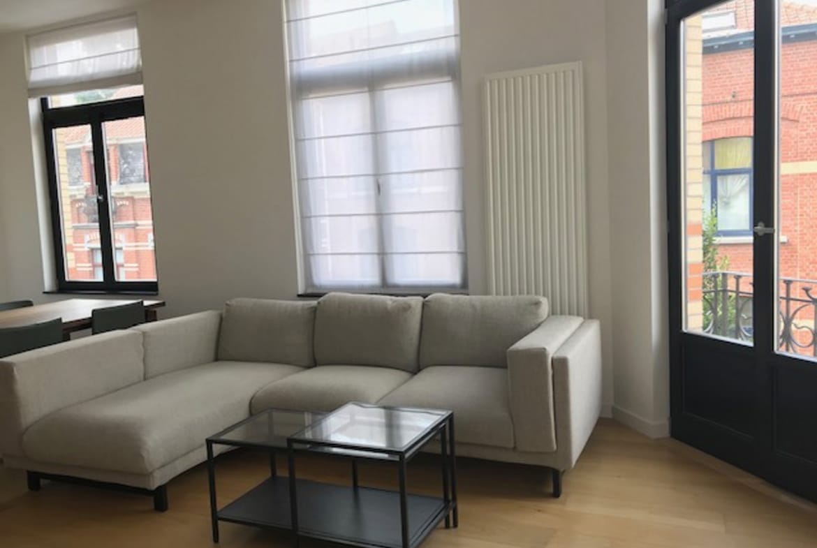 Bright living room with a white sectional sofa, glass coffee table, and large windows flooding the space with light.