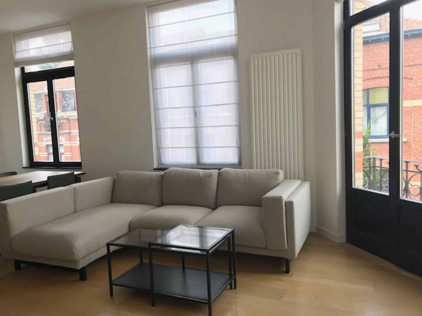 whise photo 5 Bright living room with a white sectional sofa, glass coffee table, and large windows flooding the space with light.