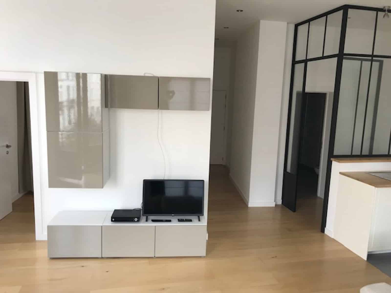 whise photo 2 Modern living space with white glossy cabinets, TV and console on a white media unit, and a glass-paneled room divider to the right.