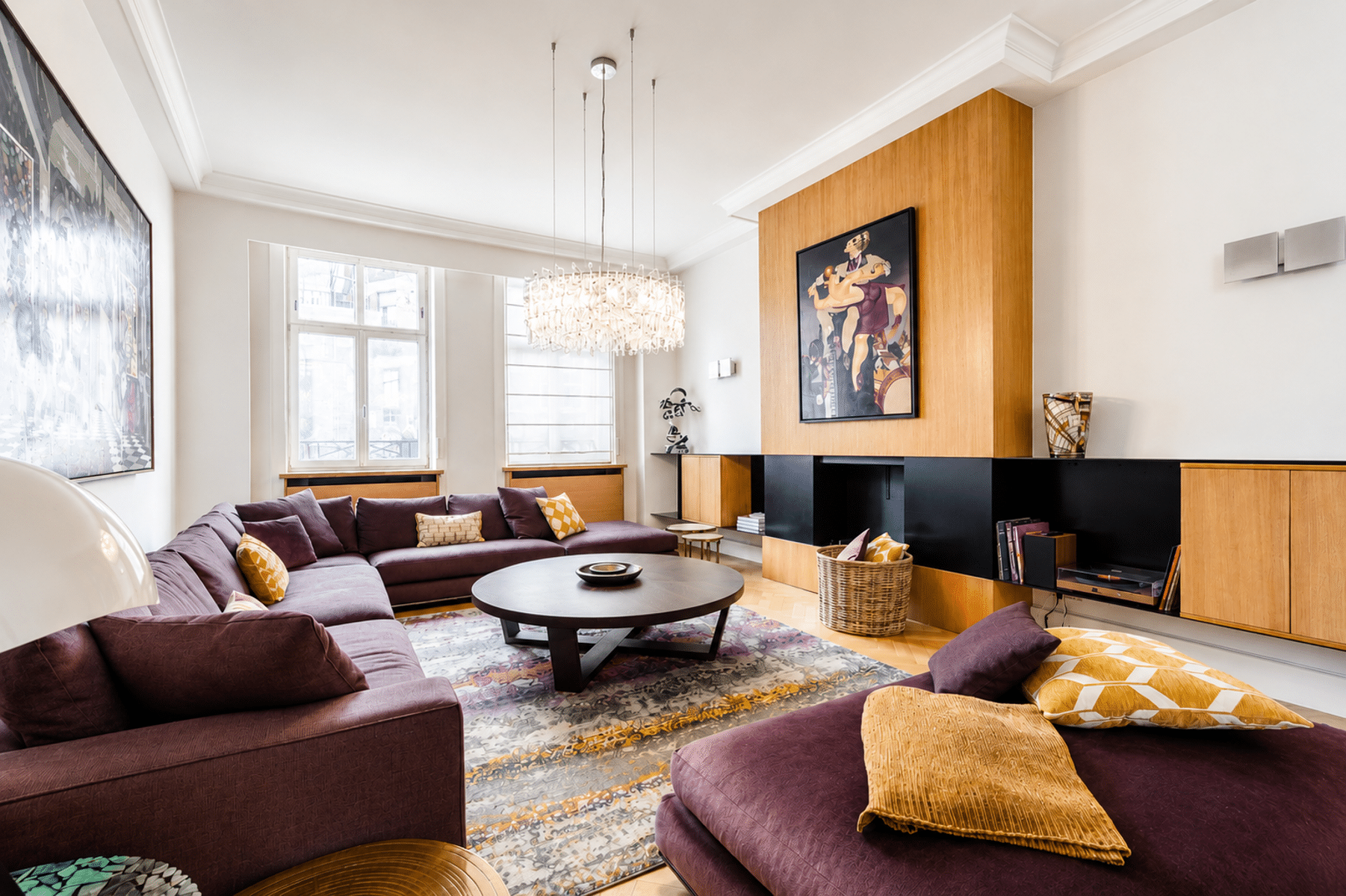 whise photo 6 Spacious living room with a purple sectional sofa, colorful throw pillows, and a round coffee table in front of a built-in wooden entertainment wall.