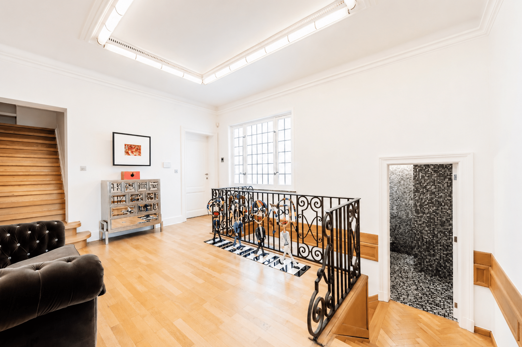 whise photo 12 Bright gallery interior with wooden stairs on the left, framed art on the wall, and a decorative railing with colorful figures along a landing.
