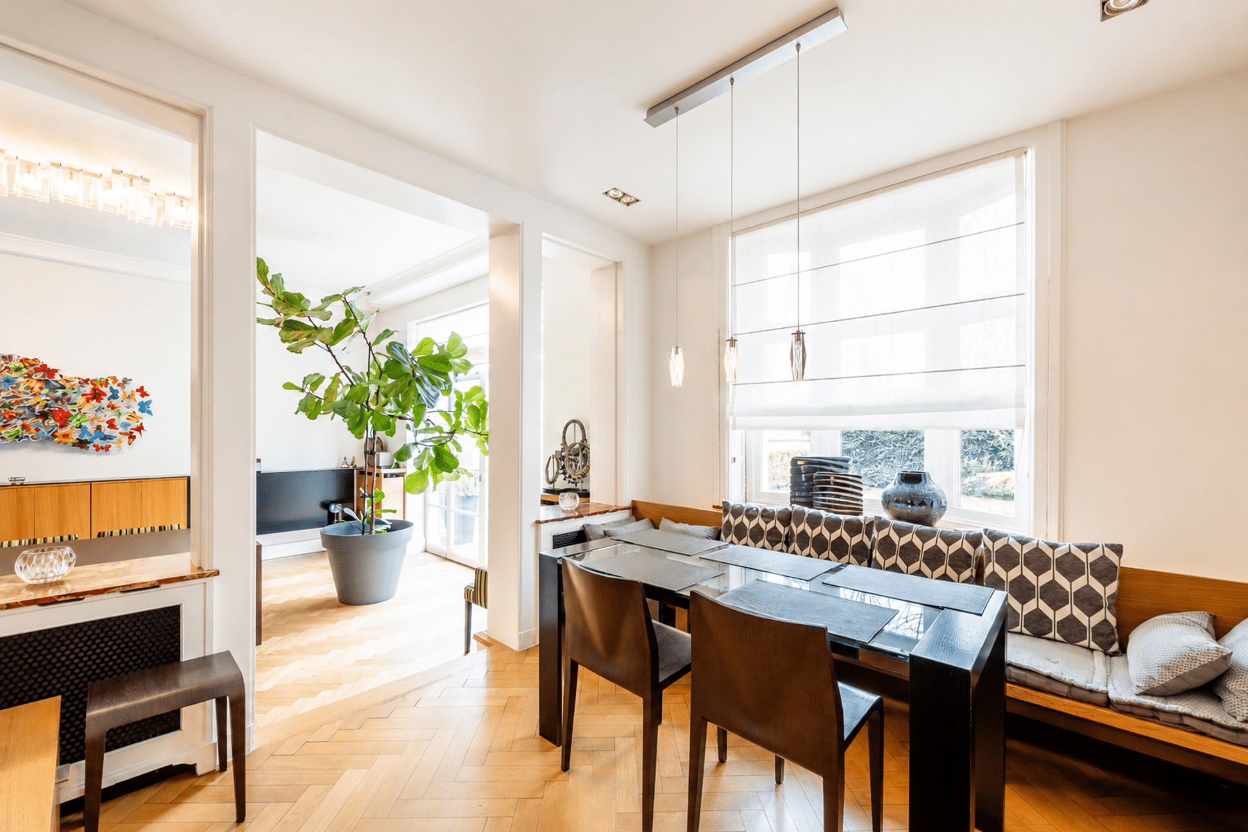 whise photo 8 Open-plan dining area with glass-top tables, dark wooden chairs, and a long patterned bench under large windows. Bright, airy space featuring a tall potted plant and contemporary pendant lighting.